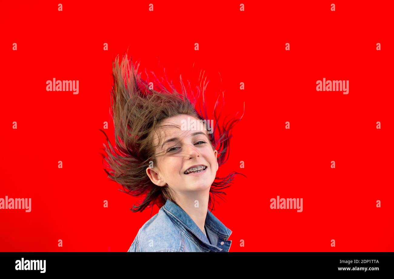 Portrait von lächelnd Teenager-Mädchen mit Zahnspangen und weht Haare Vor rotem Hintergrund Stockfoto