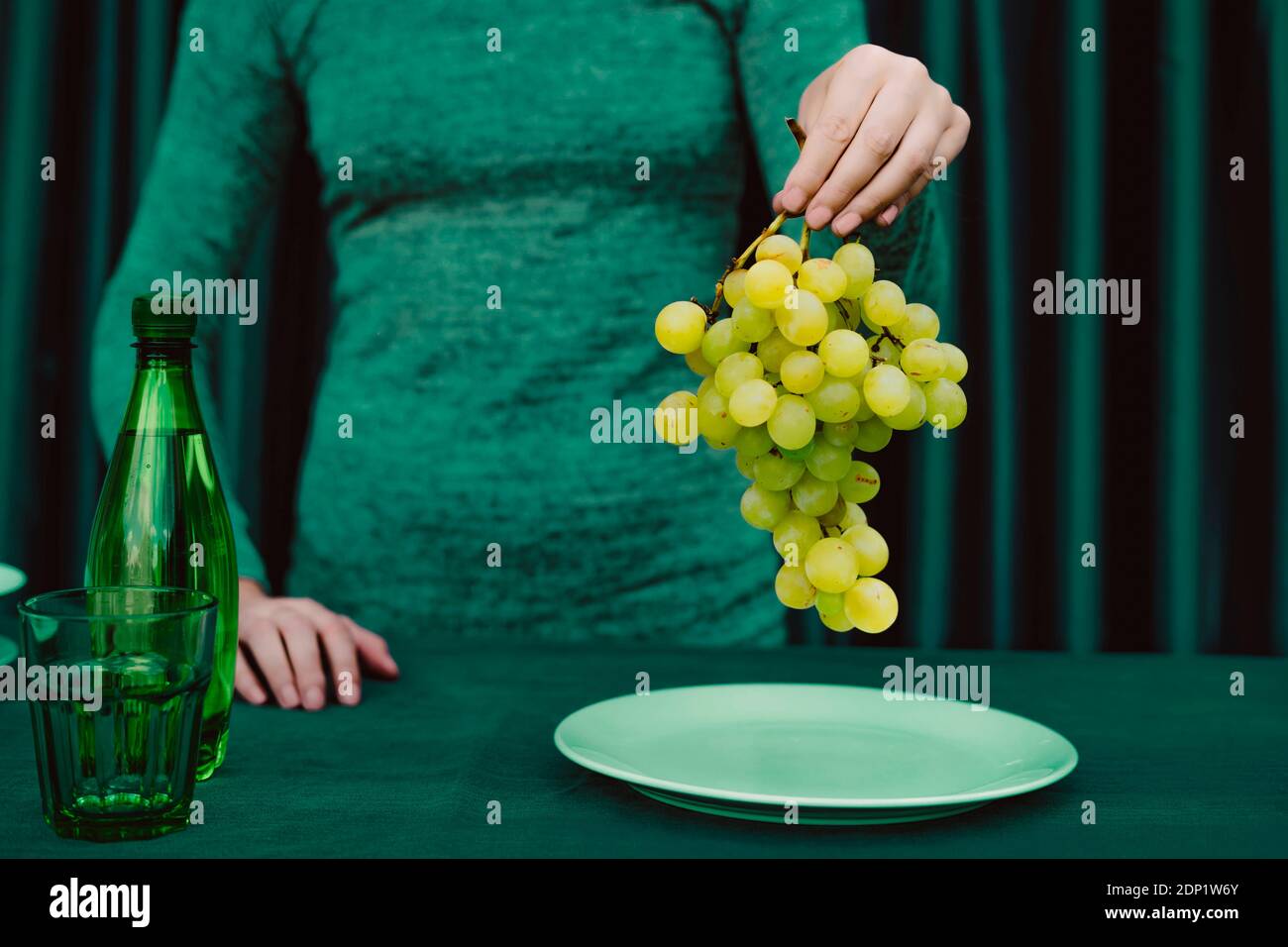 Mittelteil der Frau, die Trauben Früchte hält, während sie gegen Grün steht Vorhang Stockfoto