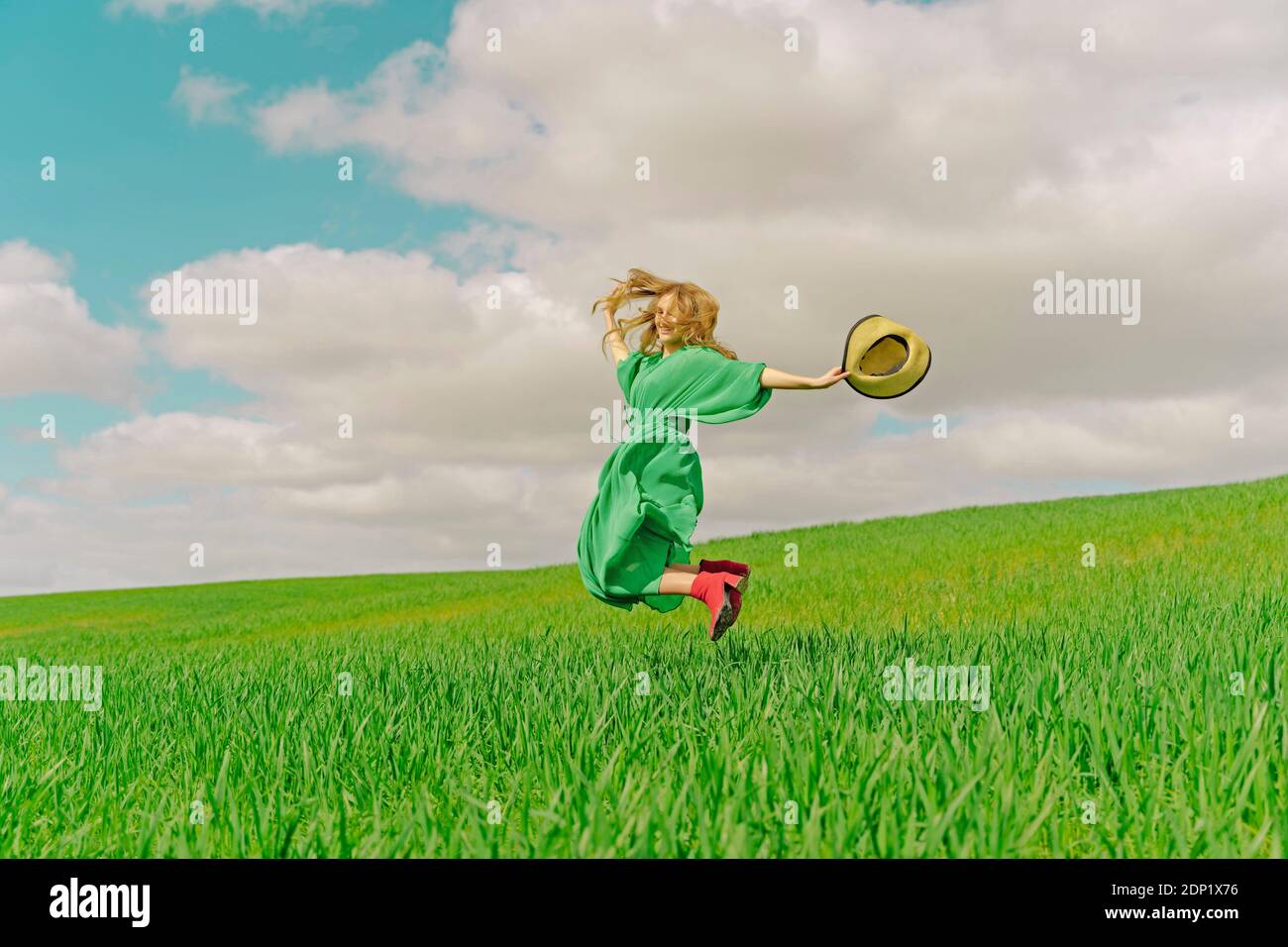 Glückliche junge Frau trägt grünes Kleid Springen in der Luft Auf einem Feld Stockfoto