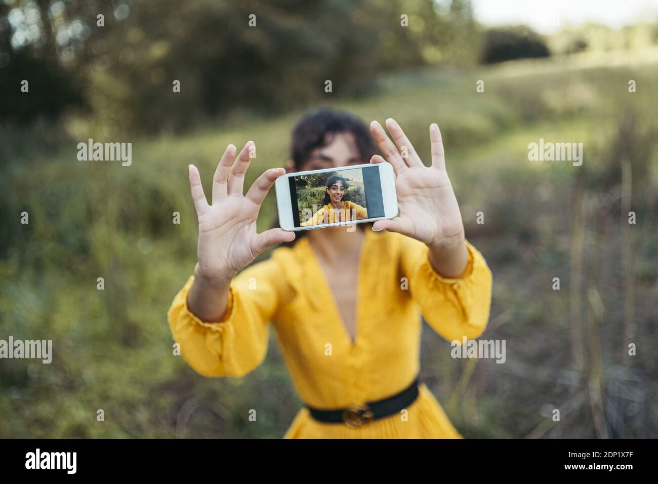 Glückliche junge Frau tragen gelbe Kleid mit einem weissen Smartphone vor ihrem Gesicht und das Nehmen eines selfie Stockfoto