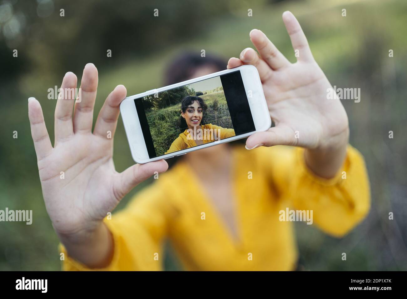 Glückliche junge Frau tragen gelbe Kleid mit einem weissen Smartphone vor ihrem Gesicht und das Nehmen eines selfie Stockfoto