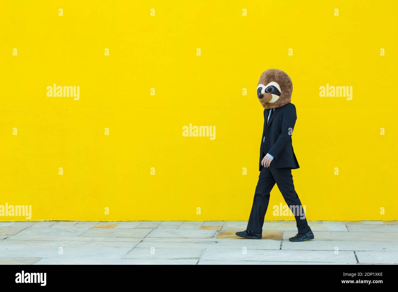 Geschäftsmann in schwarzem Anzug mit Erdmännchen Maske zu Fuß vor Der gelben Wand Stockfoto