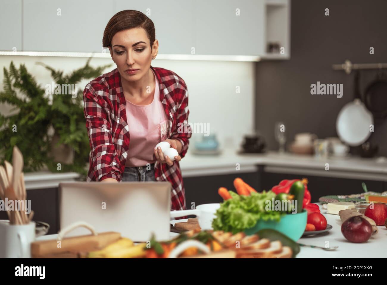 Mit einem Laptop-Computer Hausfrau Online-Rezepte suchen beim Kochen oder Backen halten Eier in der Hand. Junge Frau, die in der Küche kocht. Gesund Stockfoto