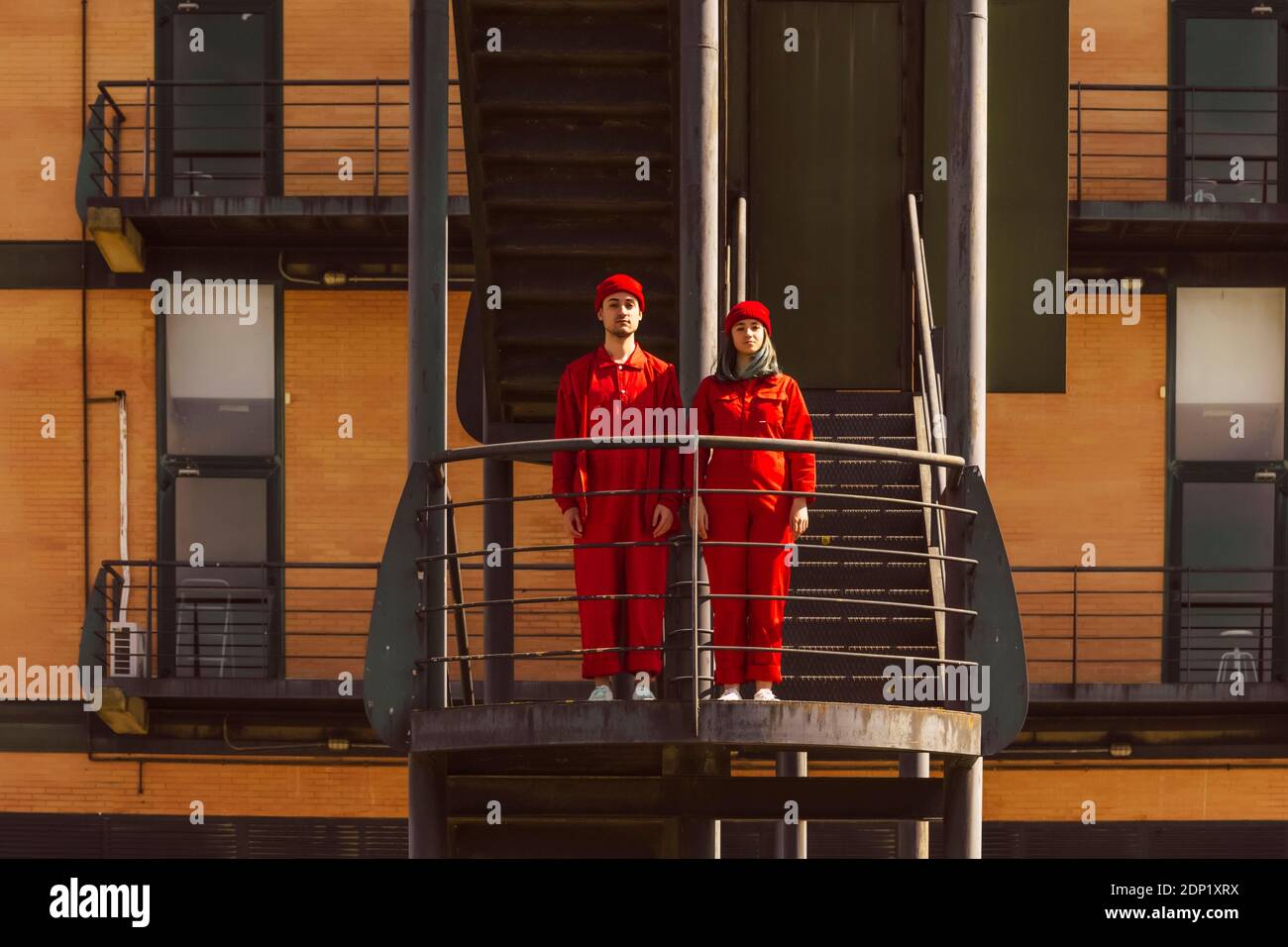 Junges Paar mit roten Overalls und Hüten, die nebeneinander stehen Seite auf Plattform Stockfoto