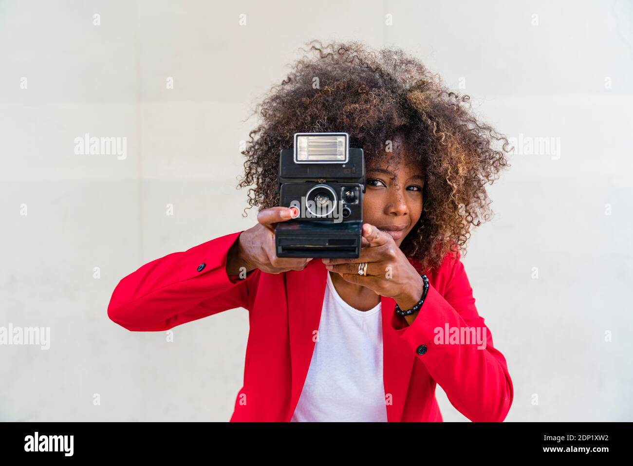 Frau, die aus der Kamera fotografiert, während sie an einer weißen Wand steht Stockfoto