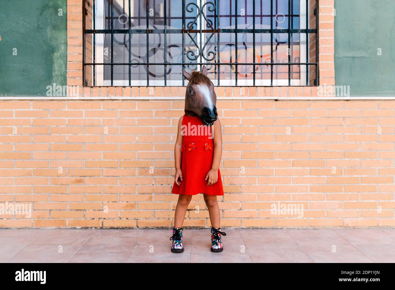 Kleines Mädchen mit einem Pferdekopf und einem roten Kleid Vor dem Haus stehen Stockfoto