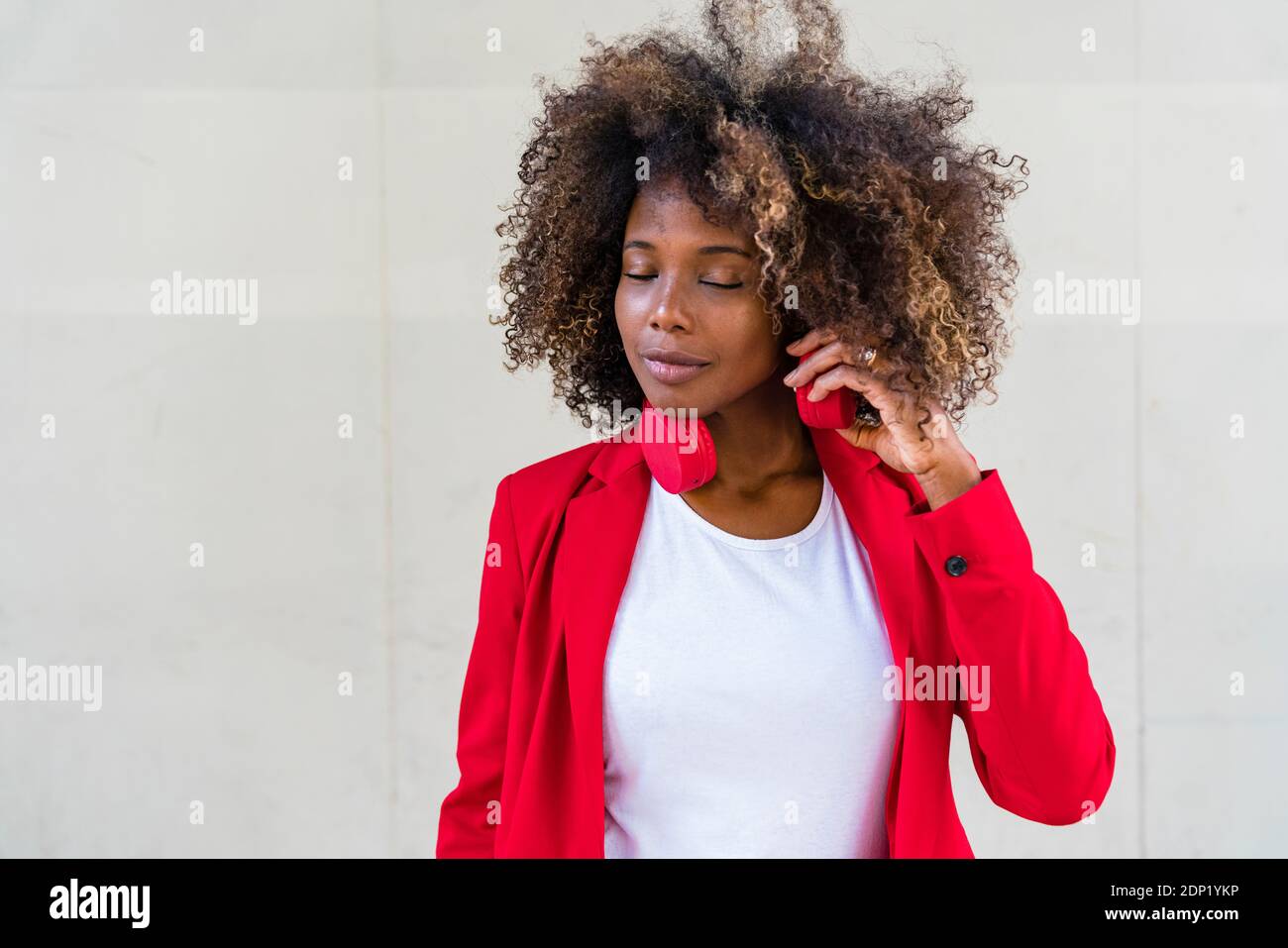 Betrachtende Frau mit Kopfhörern um den Hals, die gegen die Wand stehen Stockfoto