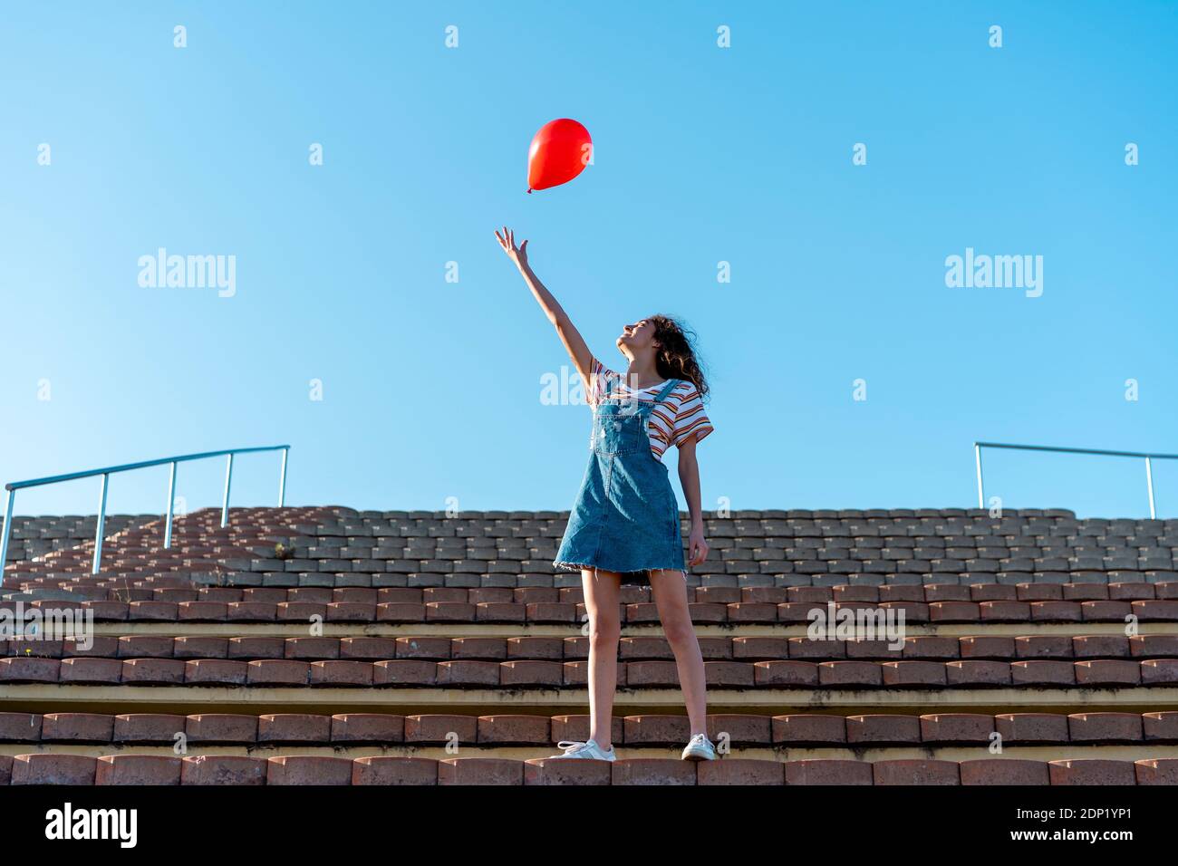 Junge Frau steht auf Tribünen, Loslassen von einem roten Ballon Stockfoto