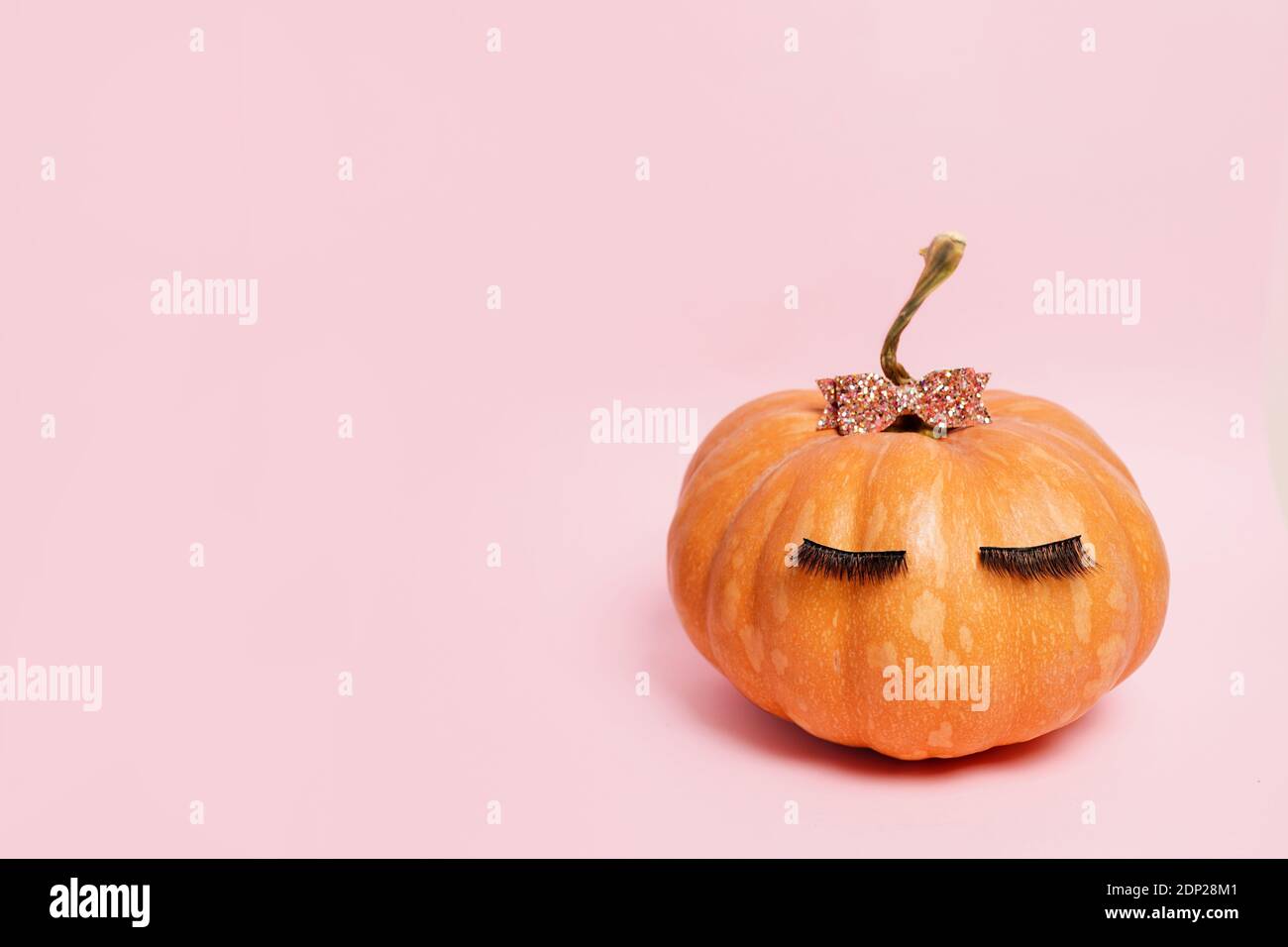 Kürbis mit falschen Wimpern und Schleife auf rosa Hintergrund. Herbst, Herbst, halloween-Konzept. Copy Space Stockfoto