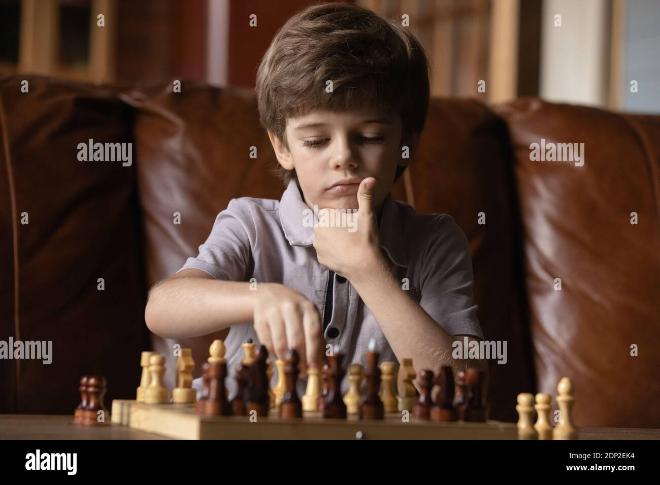 Nachdenklicher kleiner Junge sitzt auf der Couch von Schachbrett spielen Schach Stockfoto