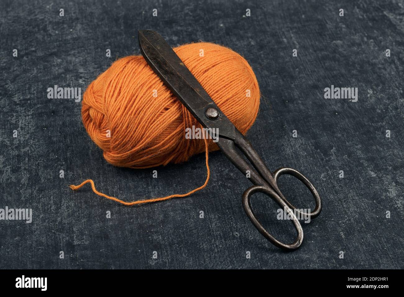 Alte rostige Schneiderschere und ein Gewirr von oranger Farbe Wollgarn in Nahaufnahme Stockfoto