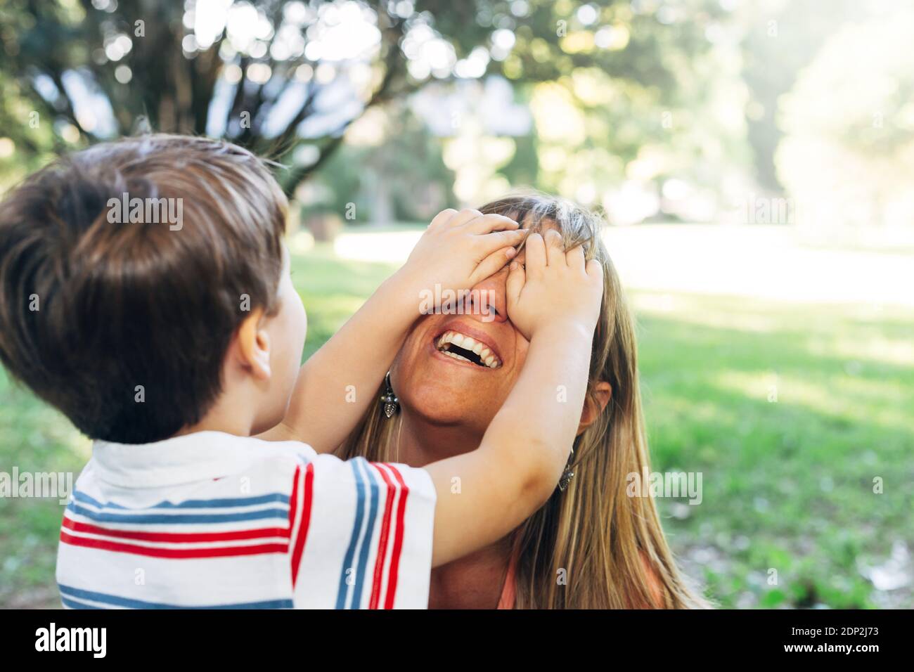 Frau spielt mit ihrem Kind. Kleiner Junge, der die Augen seiner Mutter bedeckt. Mischhäupter von al kleinen Kind immer Spaß im Park. Mutterschaft Konzept. Stockfoto