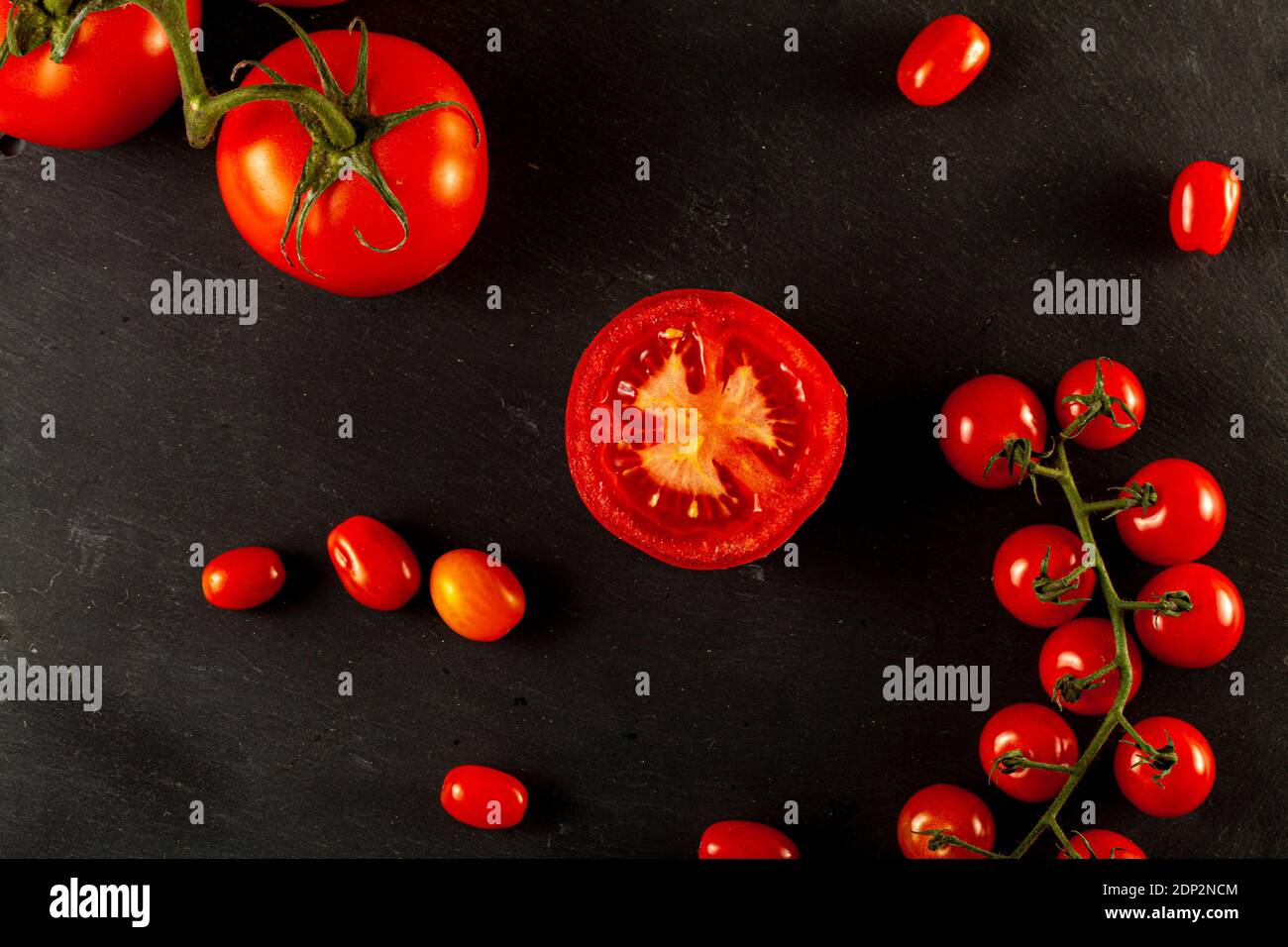 Ein flaches Lay-Bild mit einem Medley aus Tomaten auf schwarzem Holzhintergrund. Einige Roma-Tomaten und Cherry-Tomaten sind auf Reben, einer von ihnen ist in Scheiben geschnitten Stockfoto