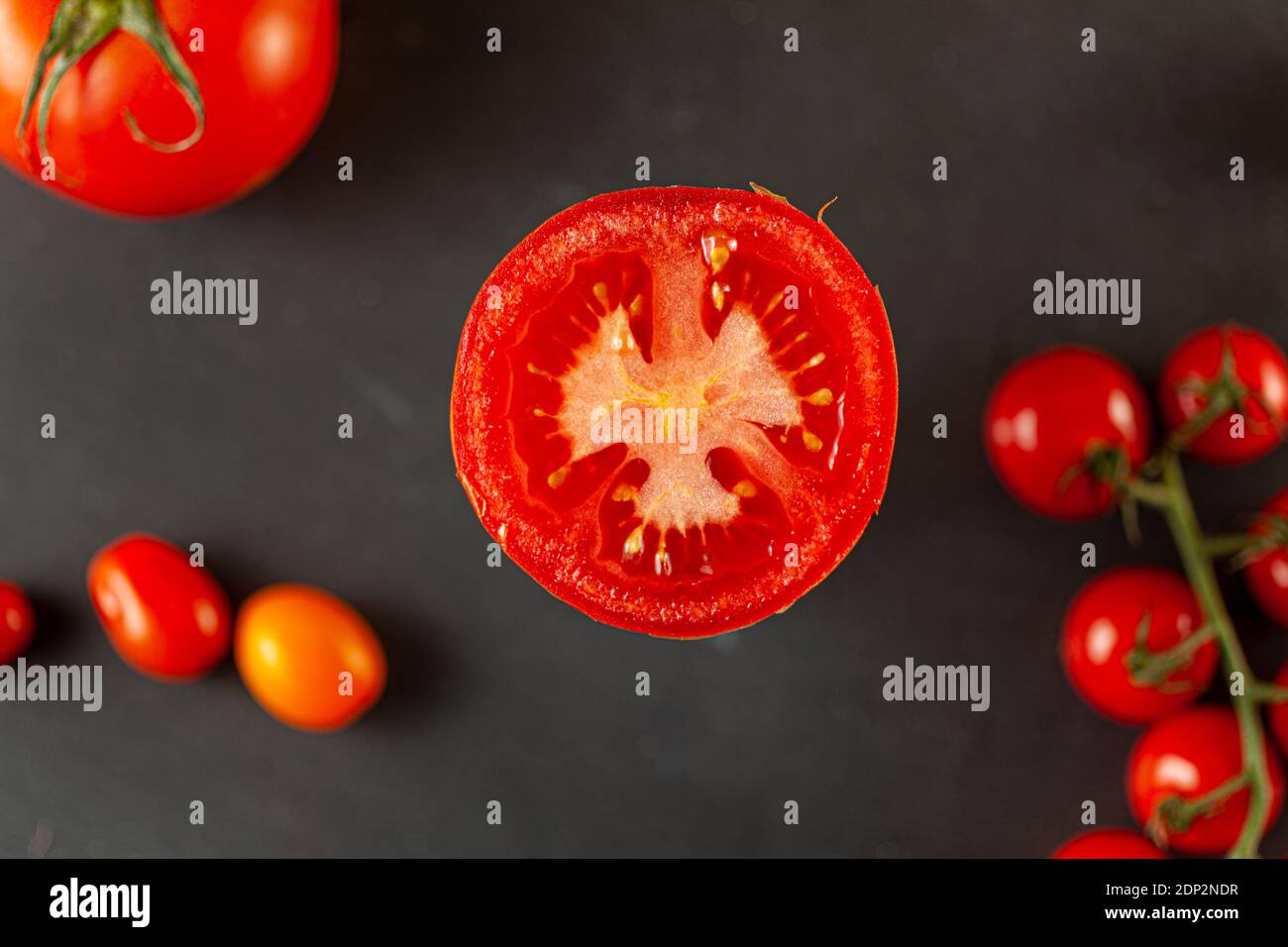 Ein selektives Nahaufnahme-Bild von oben einer geschnittenen Roma-Tomate mit Samen, die nach oben schauen. Im verschwommenen Hintergrund gibt es volle Kirsche an Stockfoto