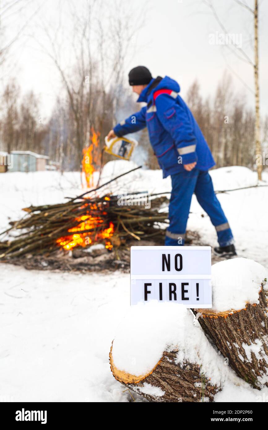 Ein Mann in blauer Uniform gießt Benzin aus einem Kanister ins Feuer. Das Konzept des Naturschutzes, Schutz vor Waldbränden, Ökologie. Stockfoto