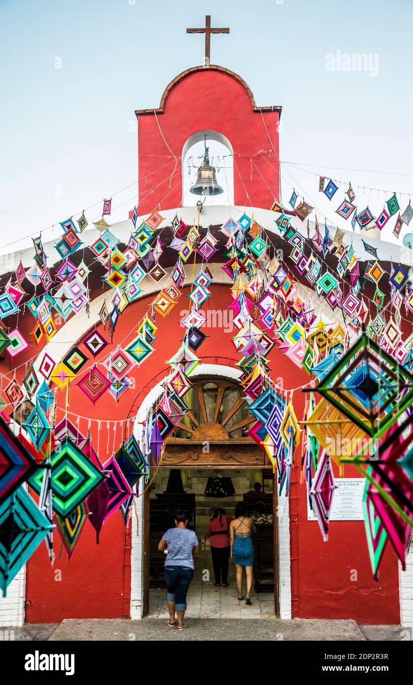 Menschen, die die Hauptkirche in Sayulita, Nayarit, Mexiko betreten, sind außen mit Ojo de Dios oder "Gottes Auge" geschmückt, einem lokalen Symbol und Handwerk der Indige Stockfoto