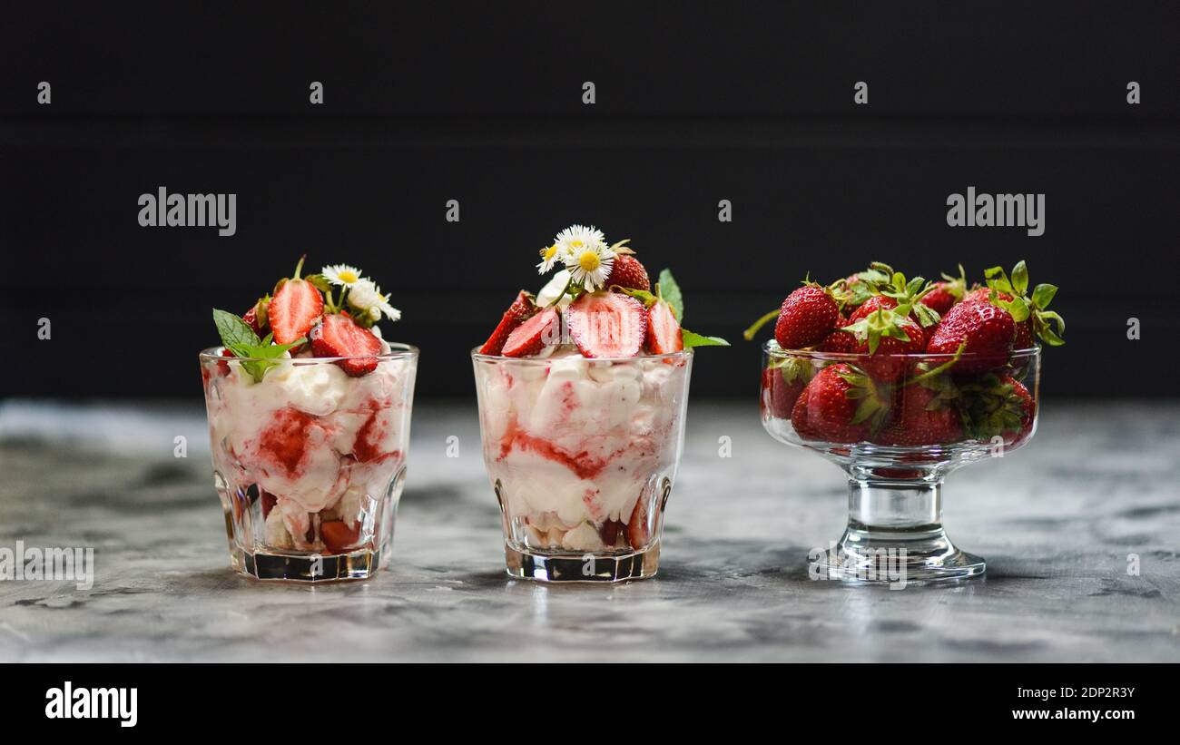 Gutes Essen. Englisches Dessert Eton Mess mit rohen Erdbeeren, Sahne und Basekues in Gläsern auf dunklem Hintergrund Seitenansicht Kopierraum Stockfoto