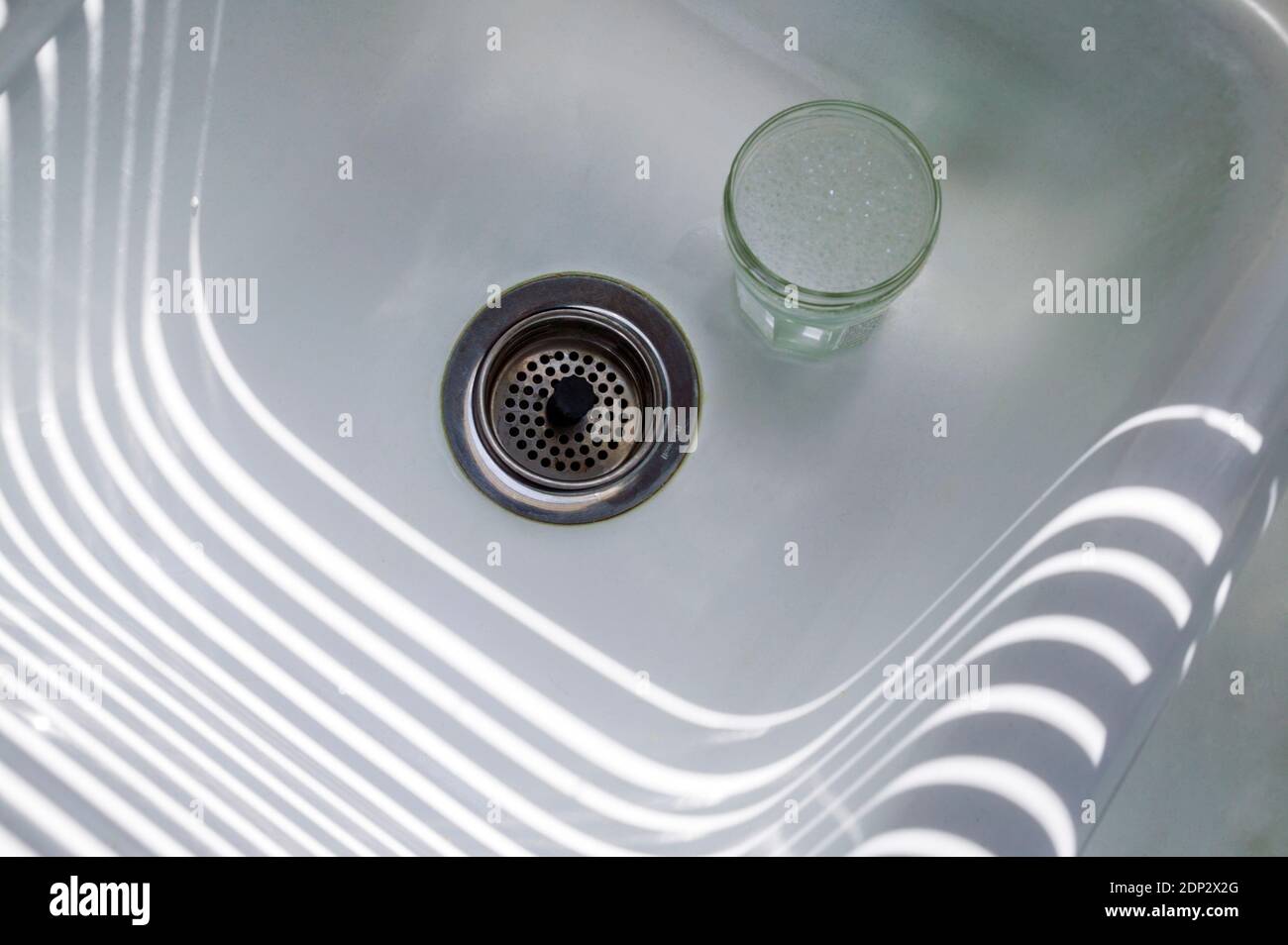 Sonnenlicht, das durch jalousien strömt, erzeugt Muster auf einem Küchenwaschbecken. Stockfoto