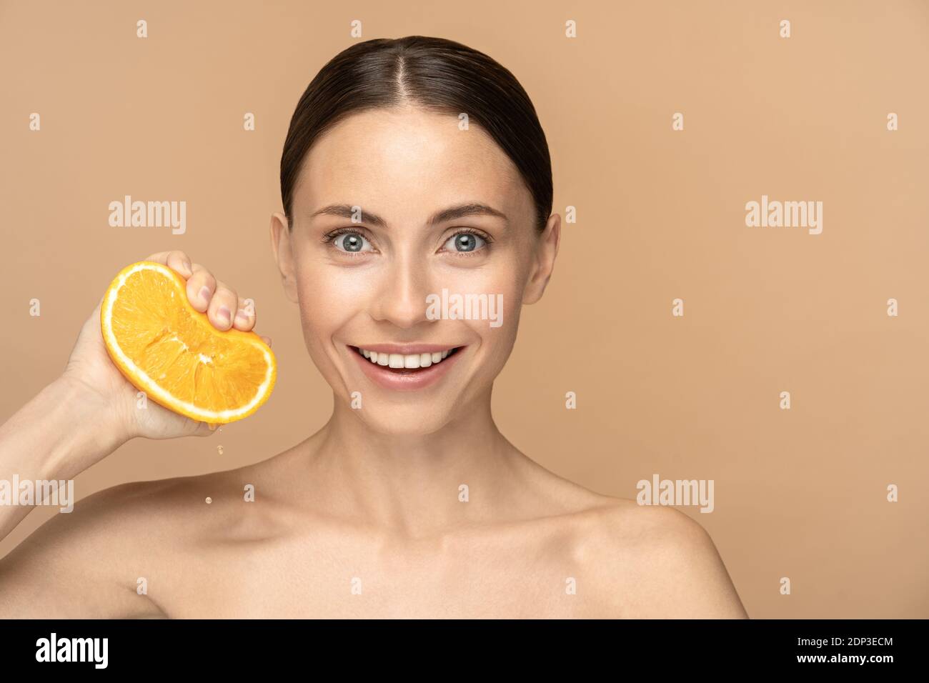 Frau mit perfekter Gesichtshaut, gekämmte Haare, quetschen orange. Lächelndes Weibchen mit natürlichem Make-up und Zitrusfrüchten auf beigem Hintergrund. Vitamin C, beaut Stockfoto