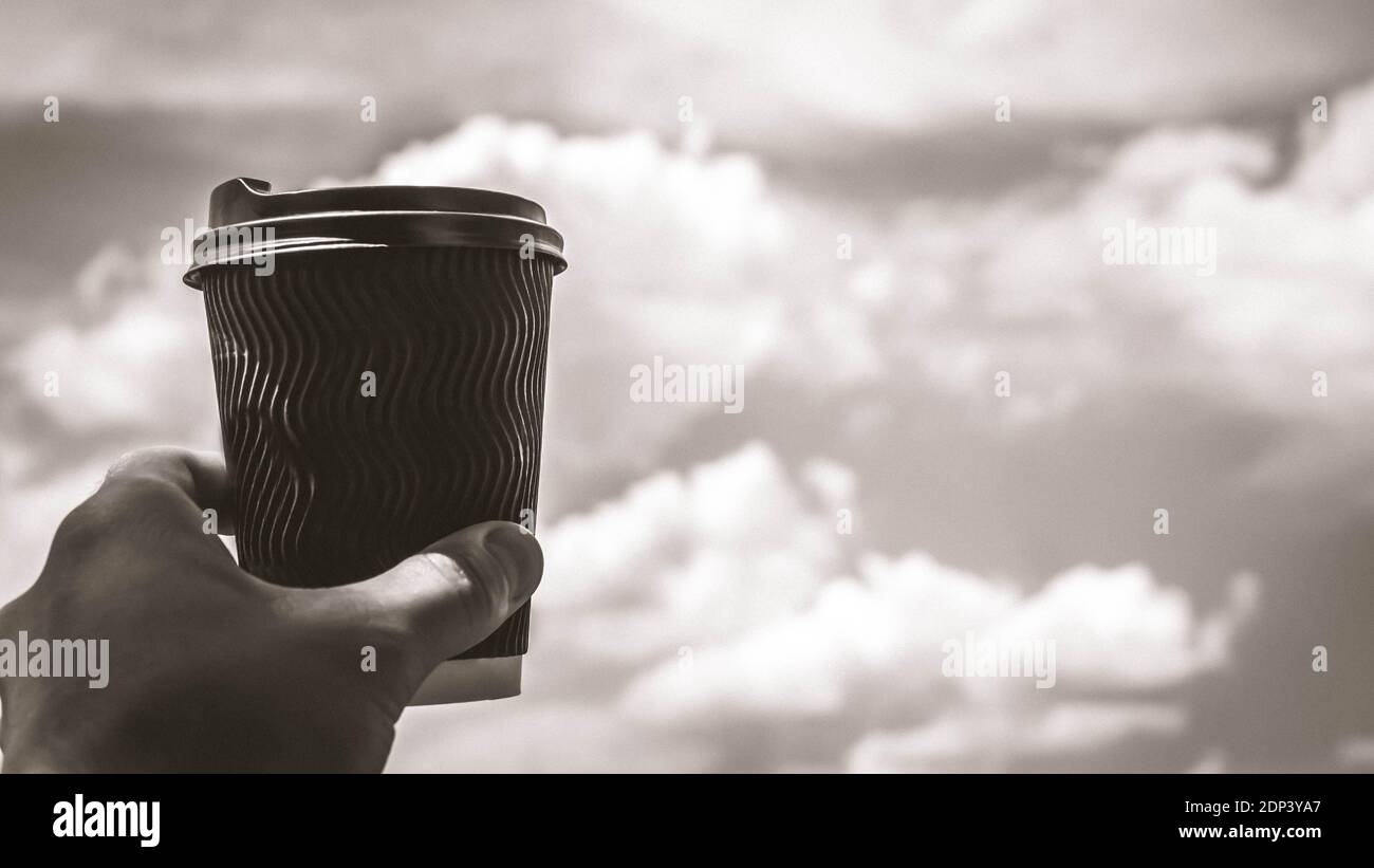 Cappuccino in der Hand eines Mannes vor dem Hintergrund des Himmels, heben Sie ein Glas, schwarzen Kaffee, Nahaufnahme, blaue Wolken und einen schönen Himmel. Stockfoto