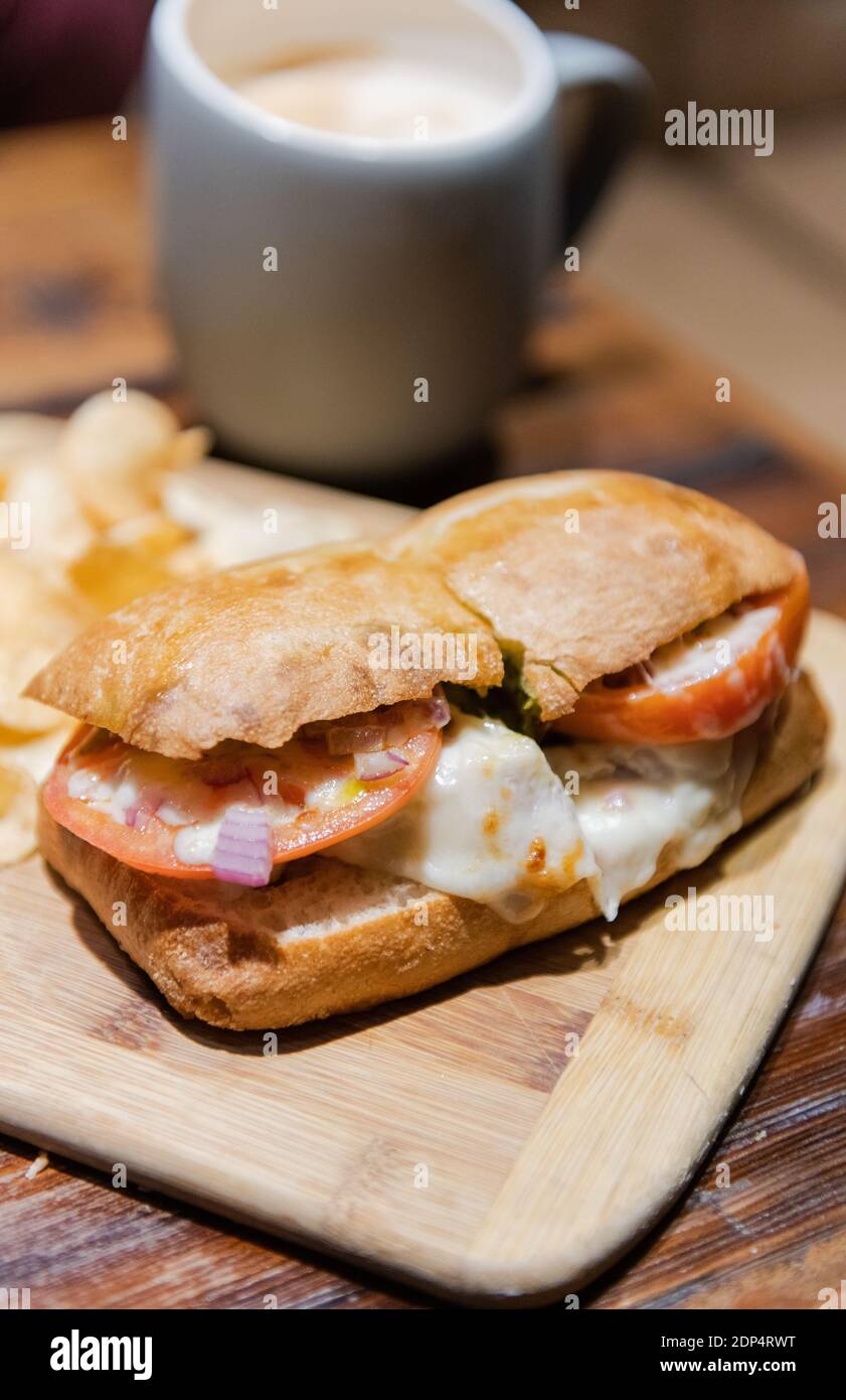Ciabatta Bread Sandwich mit Putenpesto, geschmolzenem Käse, Tomaten, Chips und einem frisch gebrauten ausgedrückten Getränk in einem Becher Stockfoto