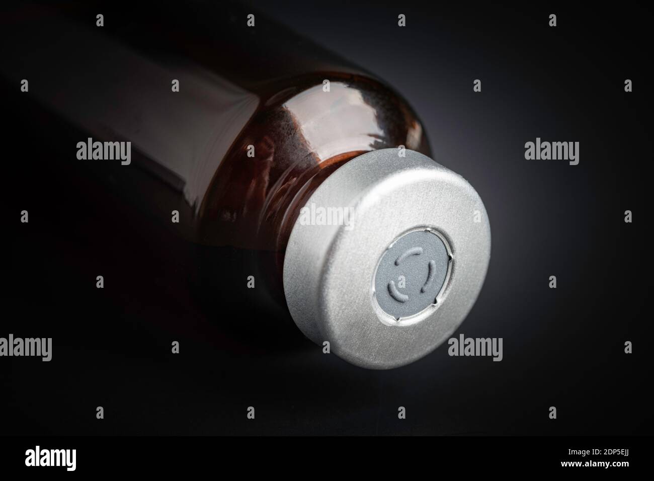 Eine Makroaufnahme mit selektivem Fokus auf einer bernsteinfarbenen Impfstoffflasche auf einem dramatischen schwarzen Hintergrund. Stockfoto
