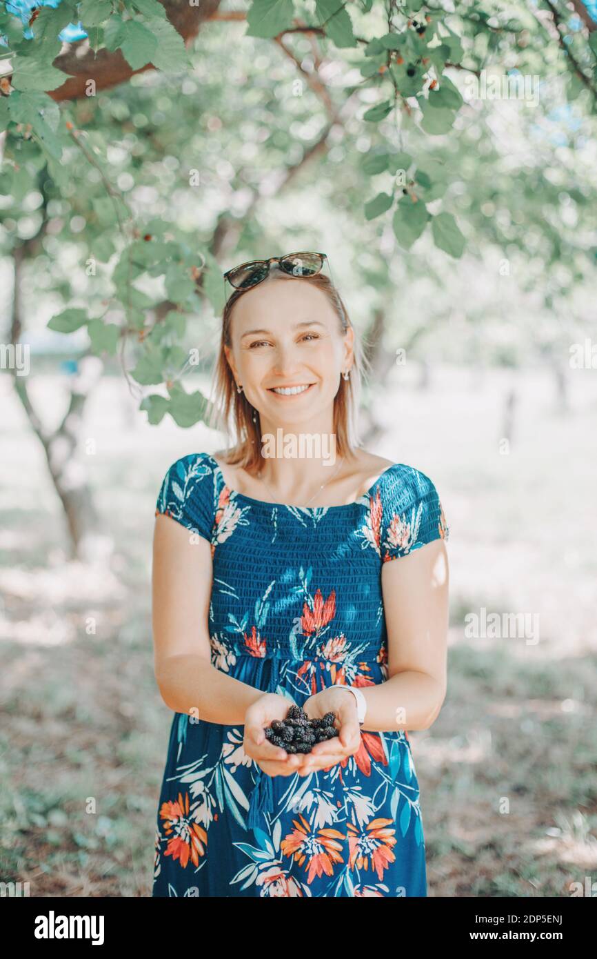 Schöne kaukasische Frau mit einer Handvoll Maulbeeren auf dem Bauernhof. Glücklicher Bauer sammeln saisonale Beeren Ernte in der Landschaft. Saisonale Lebensmittel Snack frisch Stockfoto