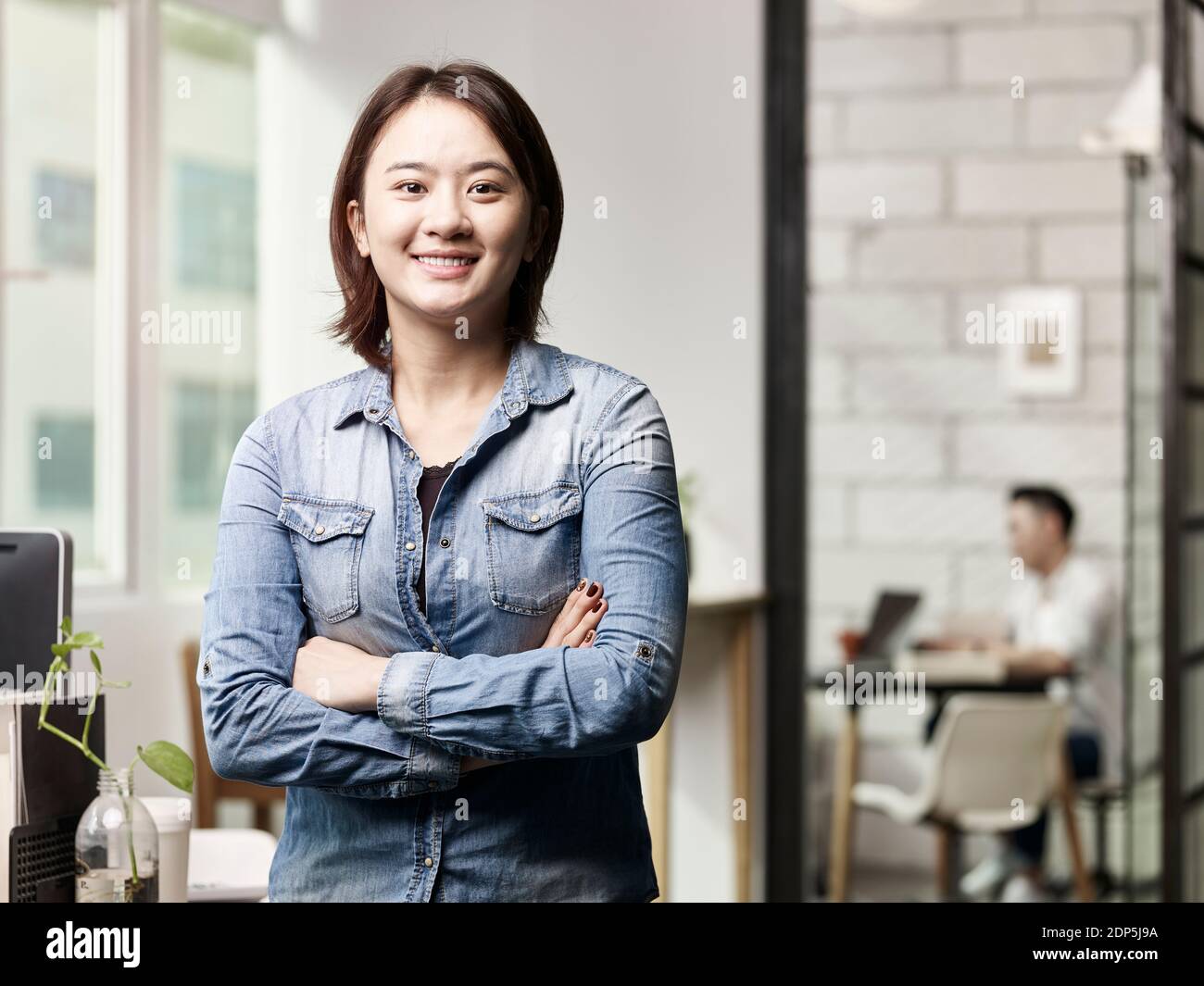 Porträt einer jungen asiatischen Geschäftsfrau, die in die Kamera schaut Lächelnde Arme gekreuzt Stockfoto