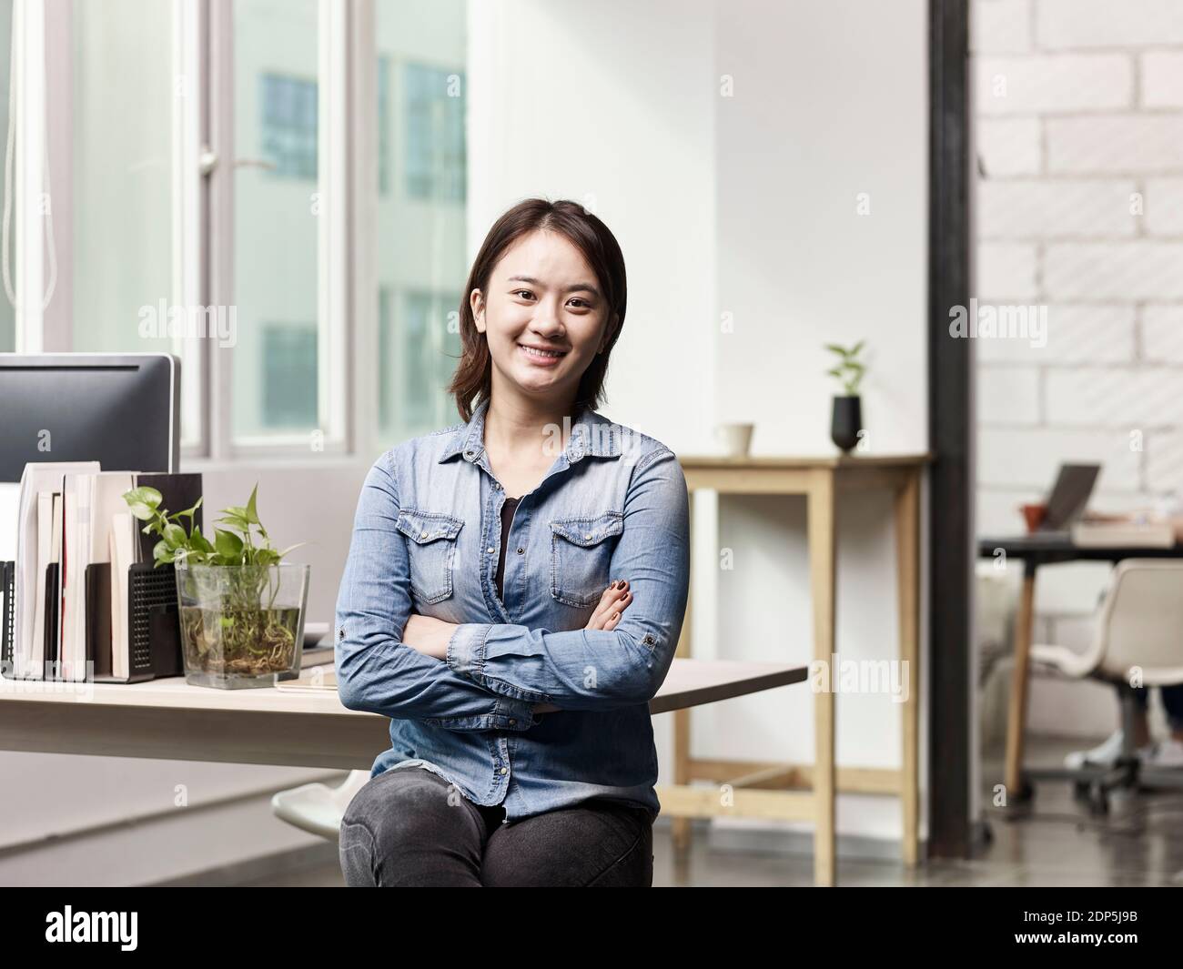 Porträt einer jungen asiatischen Geschäftsfrau, die in die Kamera schaut Lächelnde Arme gekreuzt Stockfoto