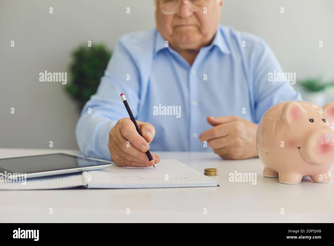 Älterer Mann im Hemd in der Brille sitzend mit Rechner und sparschwein für Sparungen und Notizen Stockfoto