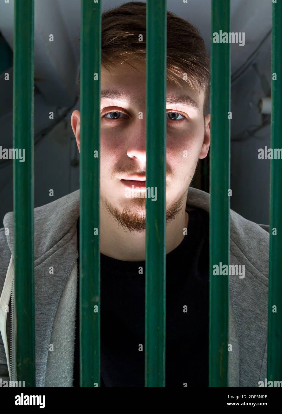 Junger Mann in einer Zelle hinter Gittern eingesperrt Stockfoto