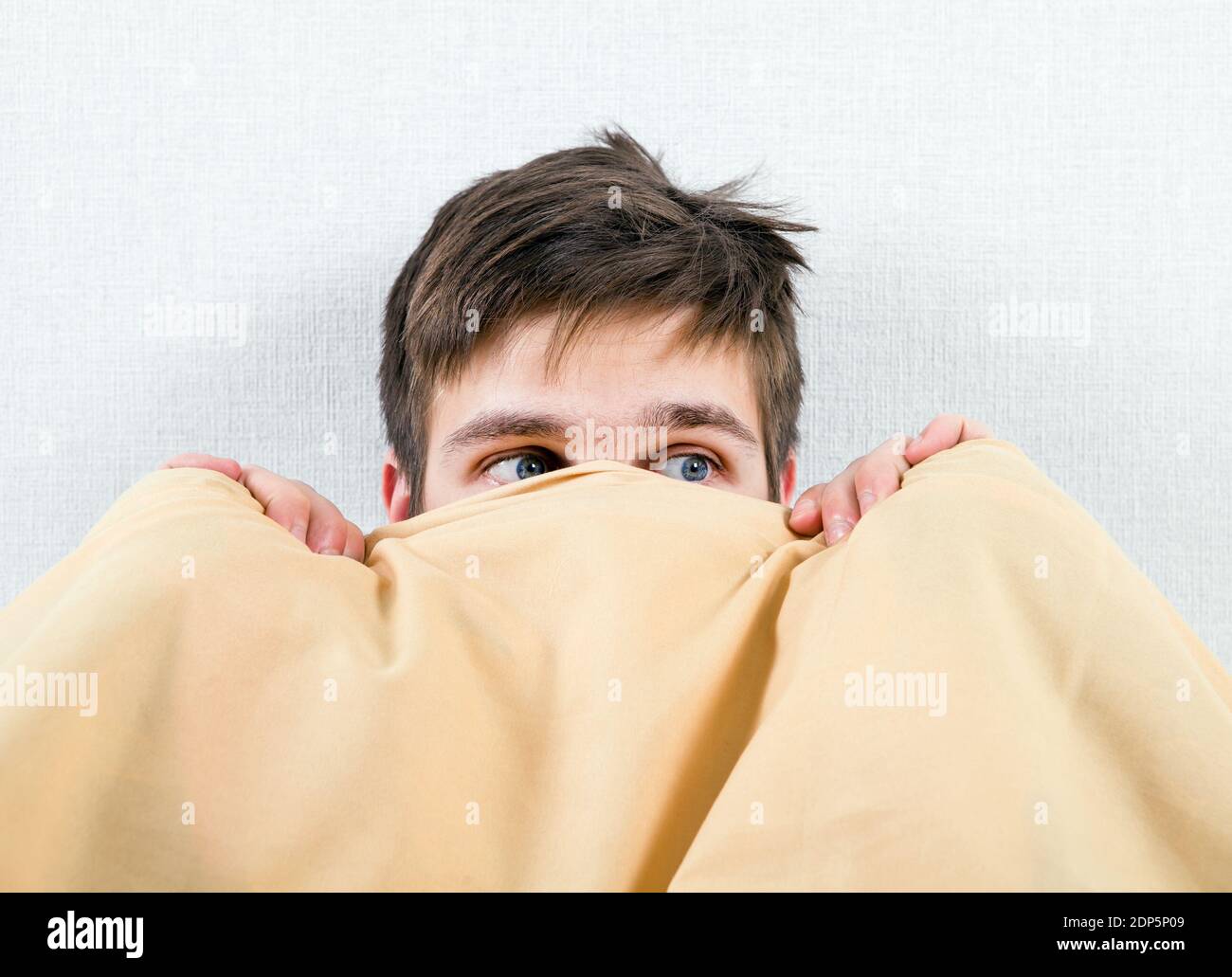 Erschrockener junger Mann unter Decke im Bett bei der Zu Hause Stockfoto