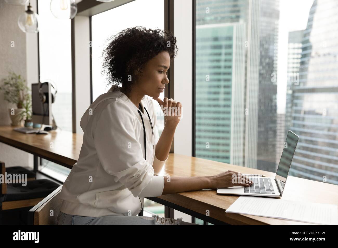 Pensive biracial Frau arbeiten auf Laptop im Büro Stockfoto