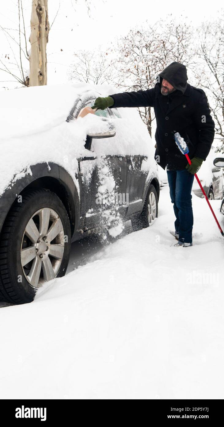 Ein Mann entfernt Schnee von einem schneebedeckten Auto. Stockfoto