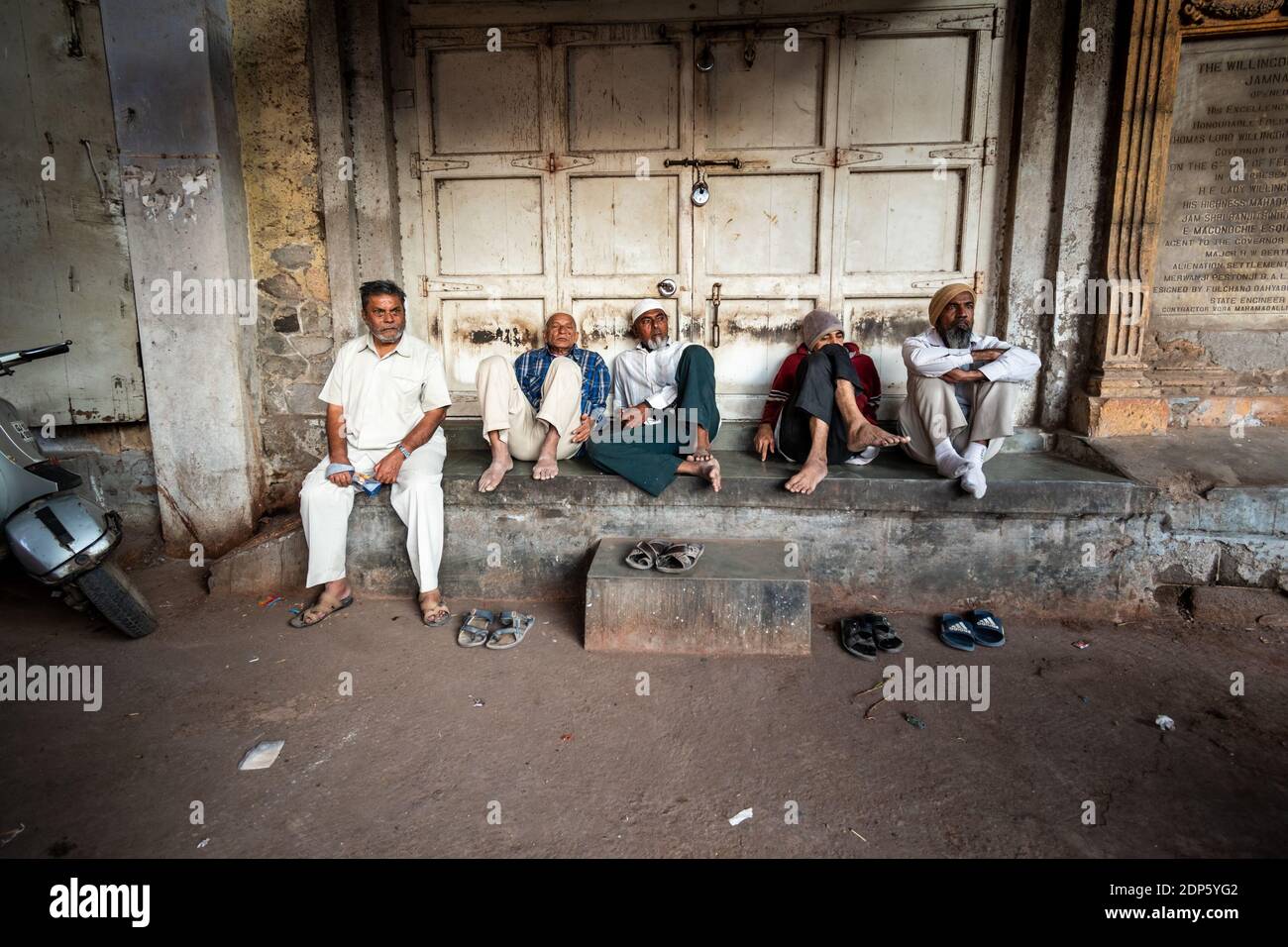 Jamnagar, Gujarat, Indien - Dezember 2018: Indische Männer sitzen ruhig auf einer Steinveranda vor einem geschlossenen Geschäft in der Altstadt. Stockfoto