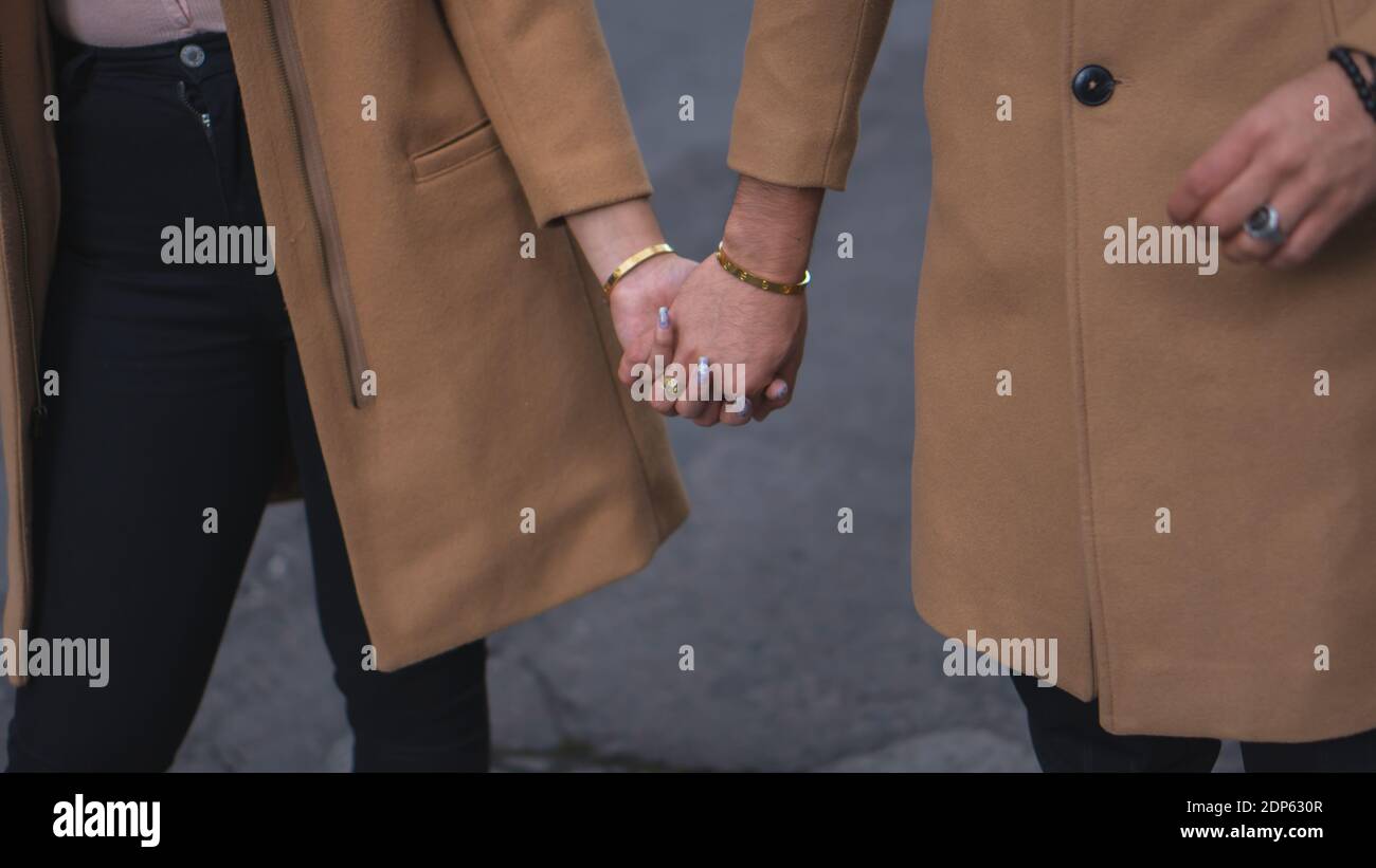 Ein liebevolles Paar, das beige Mäntel trägt und Hände hält Stockfoto