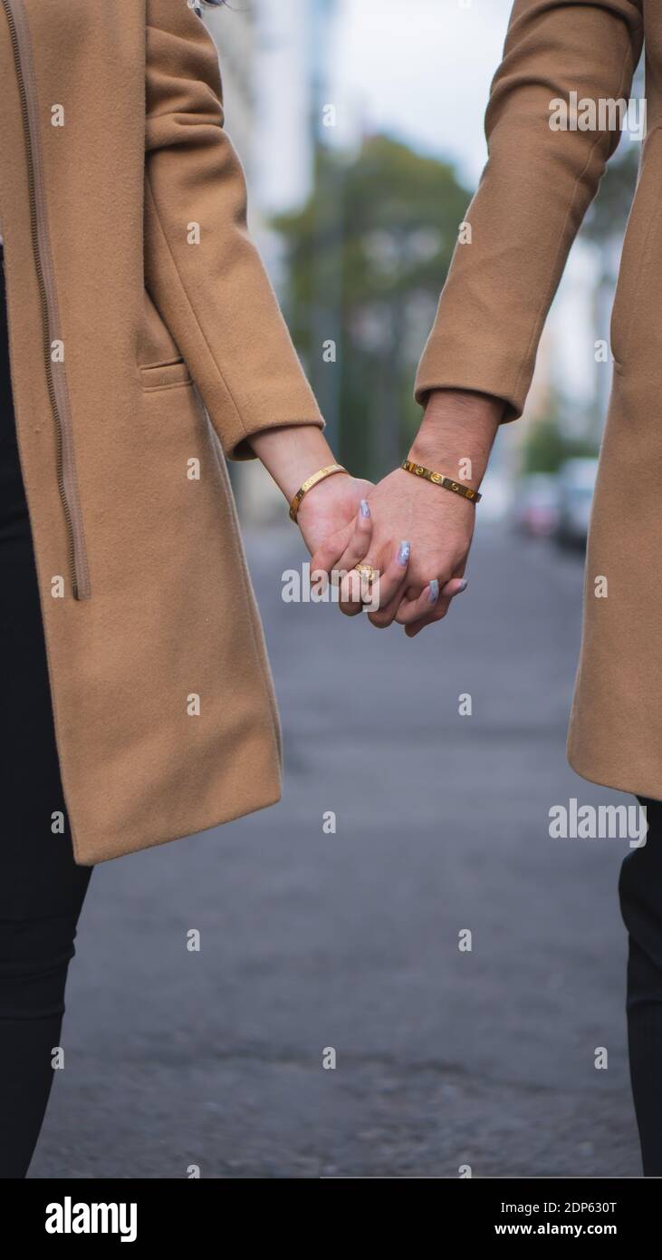Eine vertikale Aufnahme eines liebevollen Paares in beigen Mänteln Und Hände halten Stockfoto