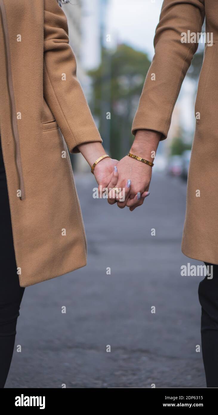 Eine vertikale Aufnahme eines liebevollen Paares in beigen Mänteln Und Hände halten Stockfoto