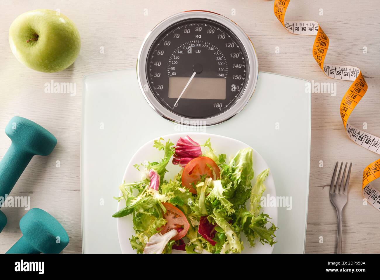 Gewichtskontrollkonzept mit Waage mit Salatplatte und Besteck auf dem Tisch und Obst, Gemüse und Sportzubehör auf dem Tisch. Draufsicht. Horizontal Stockfoto