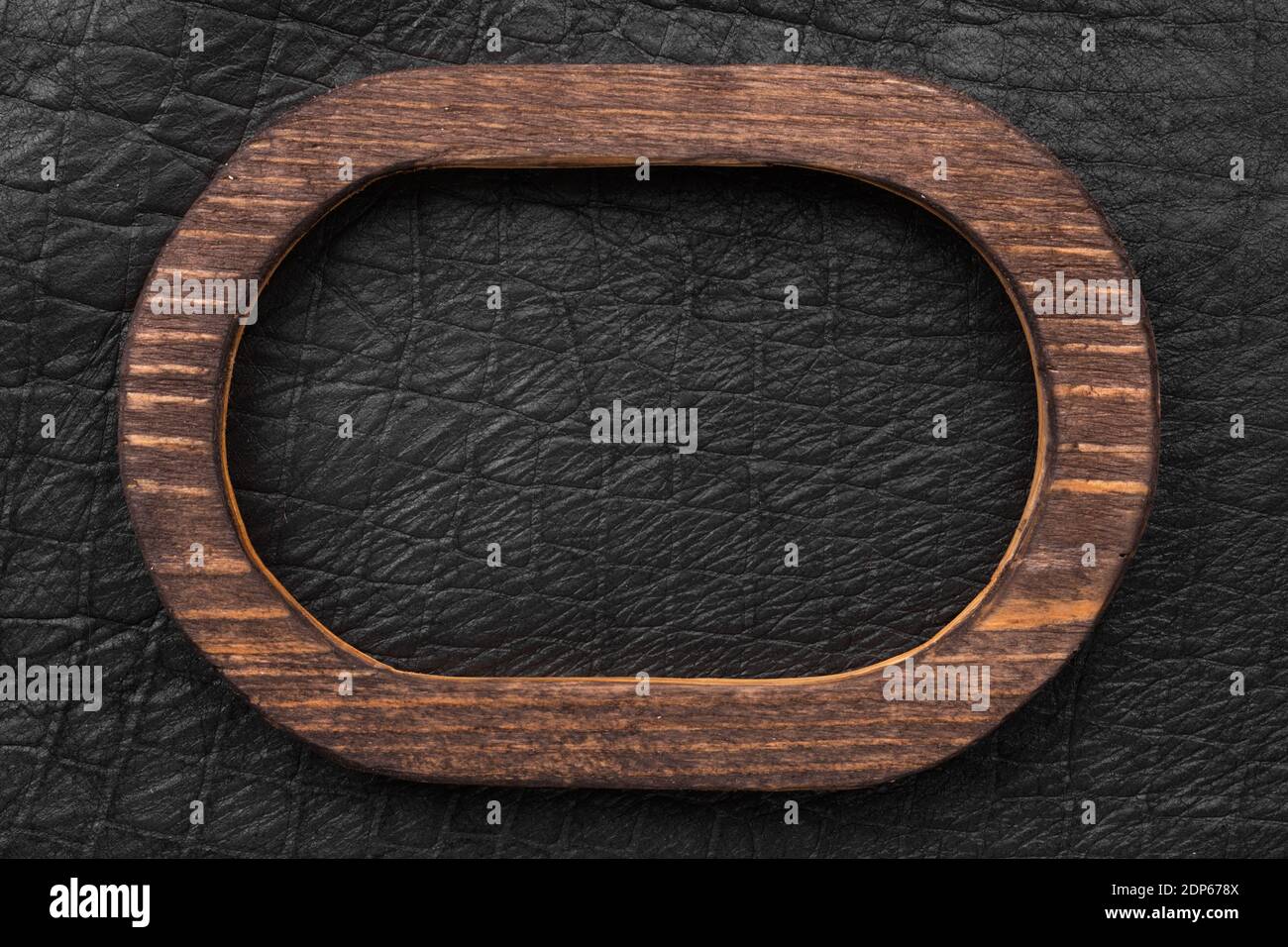 Ovaler Holzrahmen aus Holz liegt auf schwarzem Echtleder. Draufsicht. Schild, Tafel. Stockfoto