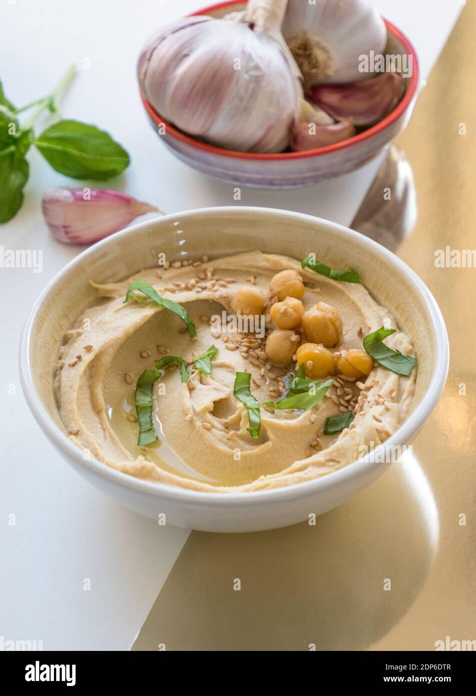 Schüssel mit frisch zubereitetem, cremigem Hummus mit Kichererbsen, Basilikum und Knoblauch isoliert auf buntem Hintergrund Stockfoto