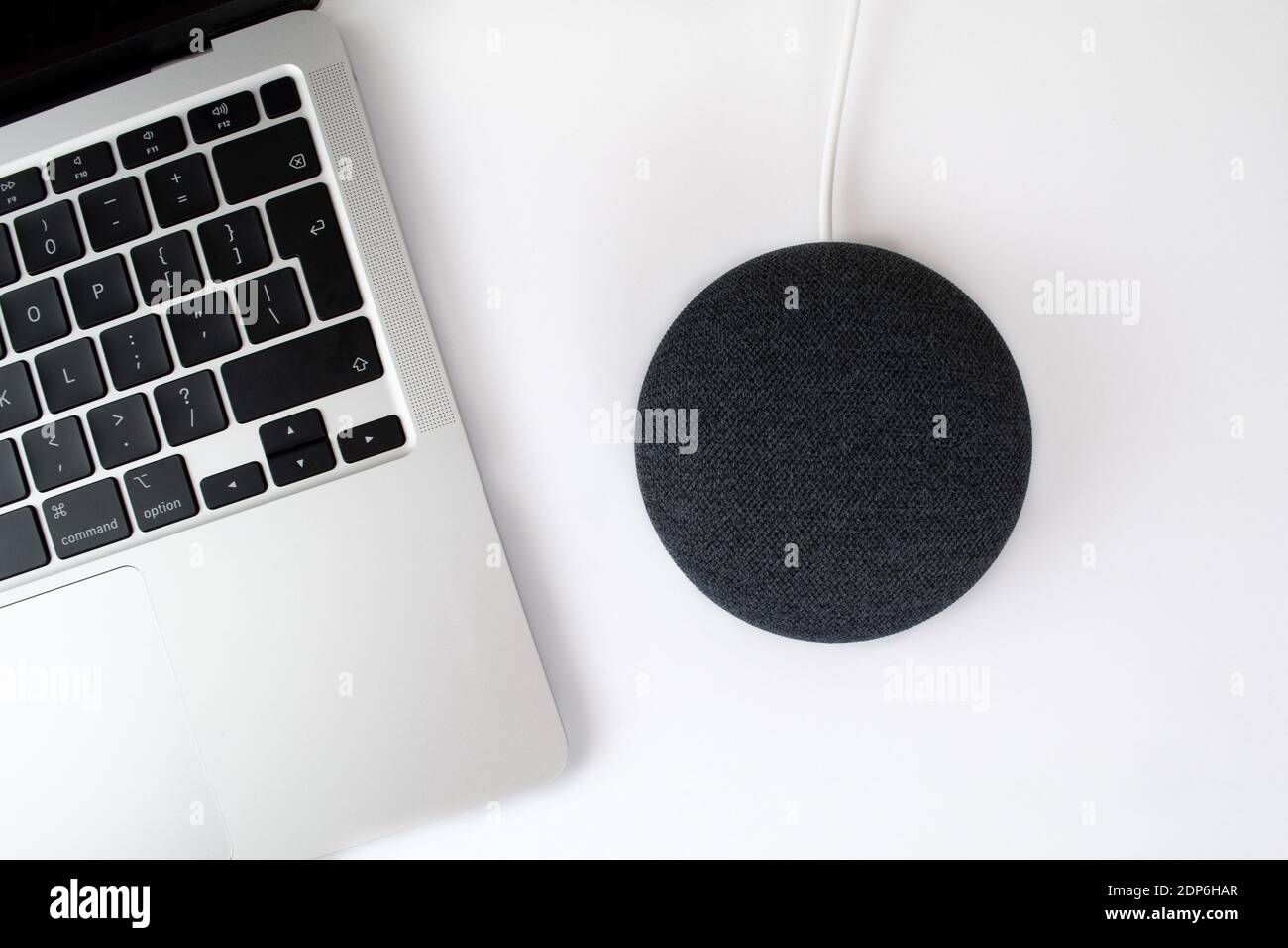London, Vereinigtes Königreich - 19. Dezember 2020: Charcoal Google Nest Home Mini Smart Speaker mit eingebautem Google Assistant neben einem Laptop-Computer. Stockfoto