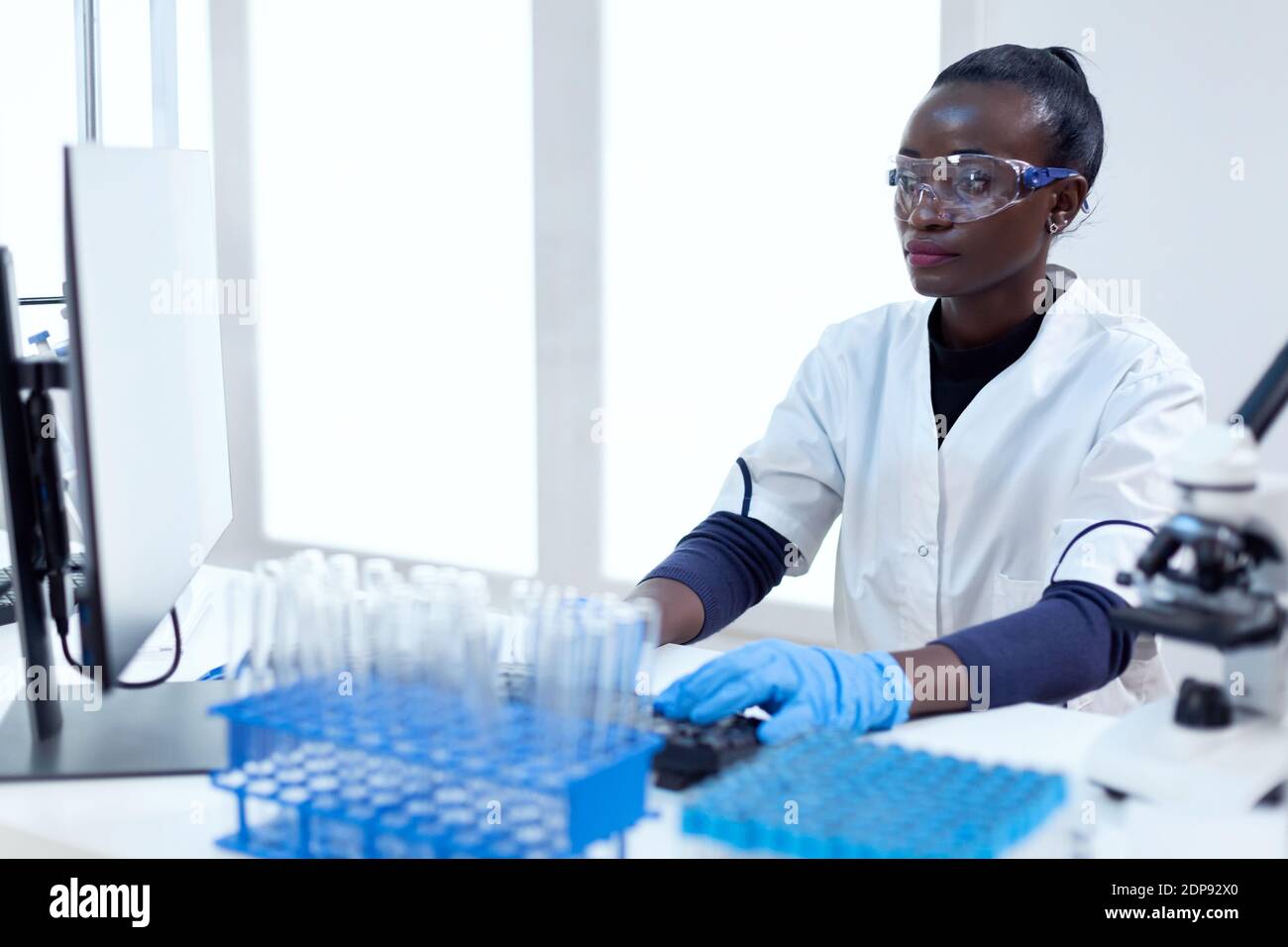Afrikanischer Biotechnologieforscher arbeitet im hellen modernen Labor mit Computer. Multiethnischer Gesundheitswissenschaftler in biochemischen Einrichtungen, der sterile Geräte trägt. Stockfoto