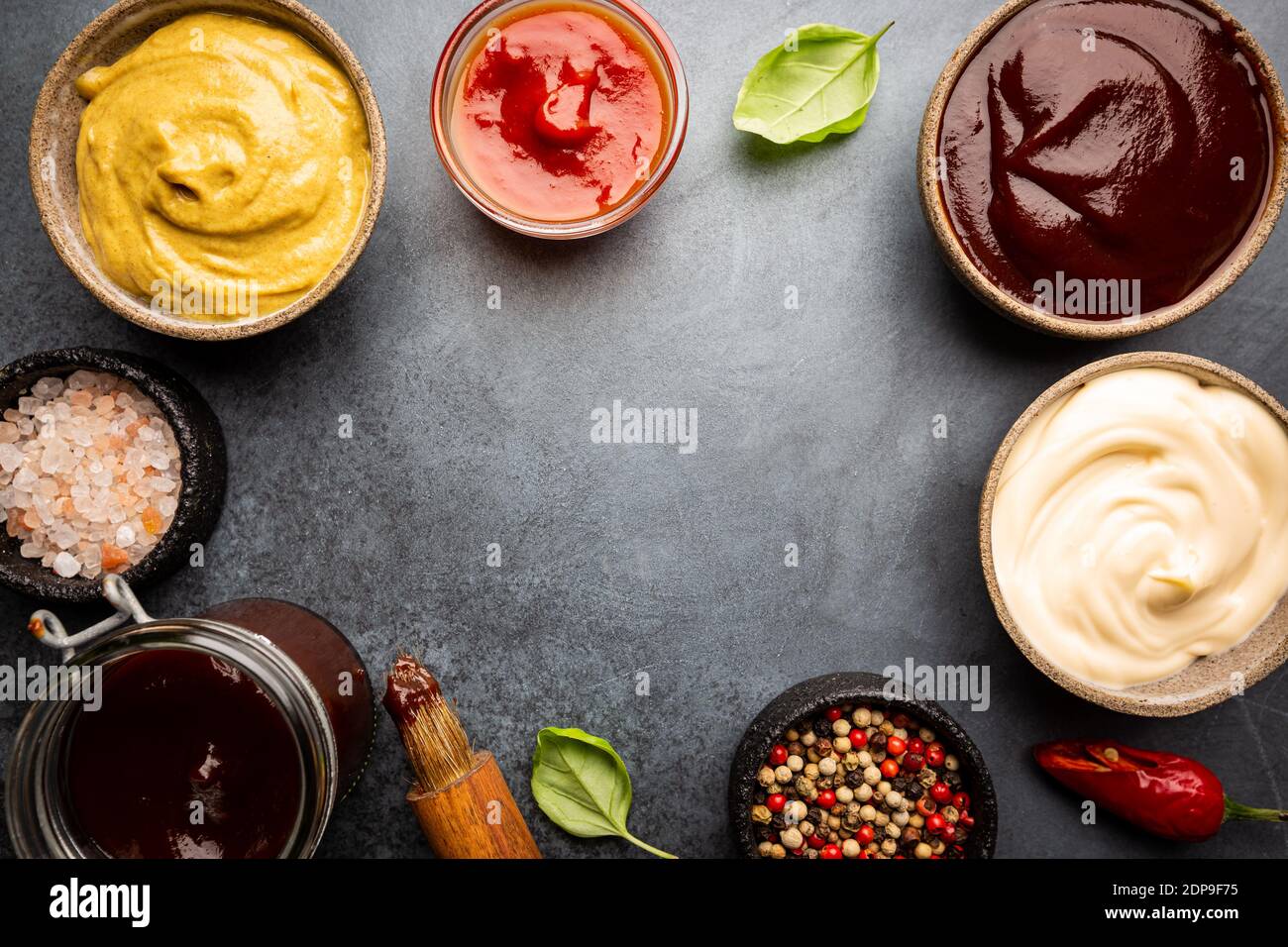 Klassische Saucen, amerikanischer gelber Senf, Ketchup, Grillsauce, Mayonnaise auf schwarzem Steinhintergrund, Draufsicht mit Kopierraum. Stockfoto