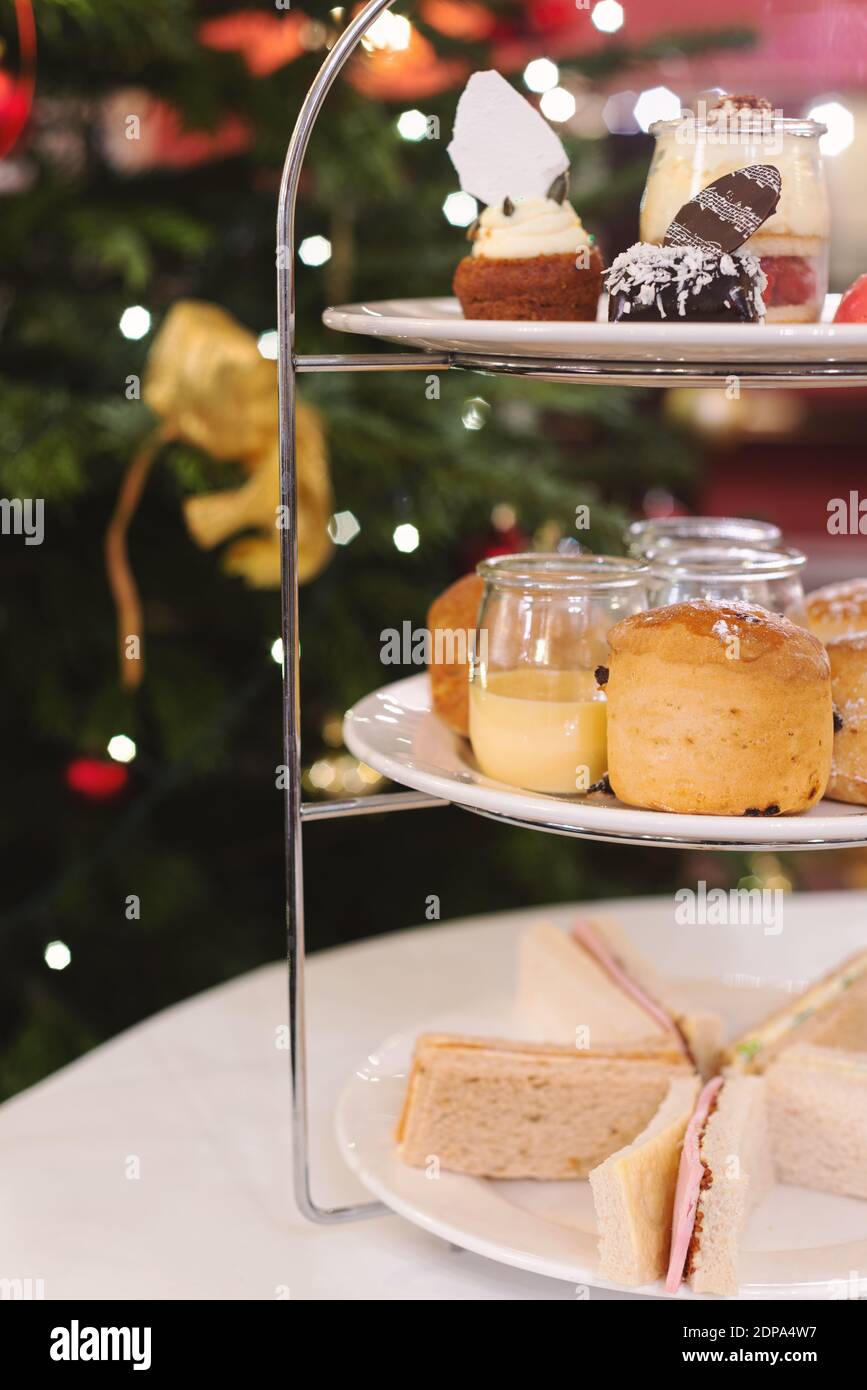 Festlicher Nachmittagstee mit Sandwiches, Scones und Puddings. Weihnachtsbaum Bokeh Licht im Hintergrund. Winter und Stimmung. Selektiver Fokus. Stockfoto