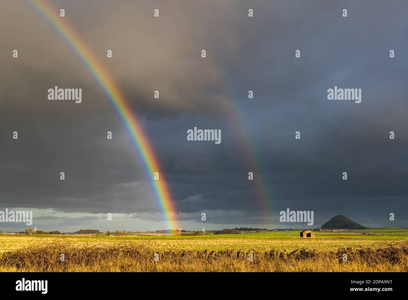 East Lothian, Schottland, Großbritannien, 19. Dezember 2020. UK Wetter: Ein auffälliger doppelter Regenbogen erscheint nach Regen und schaut in Richtung Berwick Law über Felder bei Sonnenschein Stockfoto