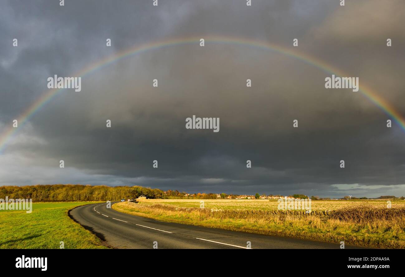 East Lothian, Schottland, Großbritannien, 19. Dezember 2020. UK Wetter: Ein auffälliger Regenbogenbogen erscheint nach Regen, der sich über eine Landstraße bei Sonnenschein wölbt Stockfoto