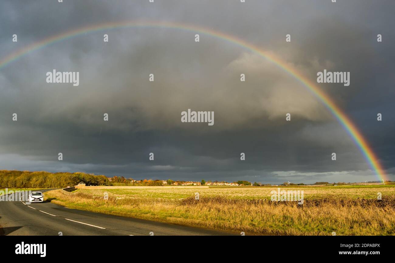 East Lothian, Schottland, Großbritannien, 19. Dezember 2020. UK Wetter: Ein auffälliger Regenbogenbogen erscheint nach Regen, der sich über eine Landstraße bei Sonnenschein wölbt Stockfoto