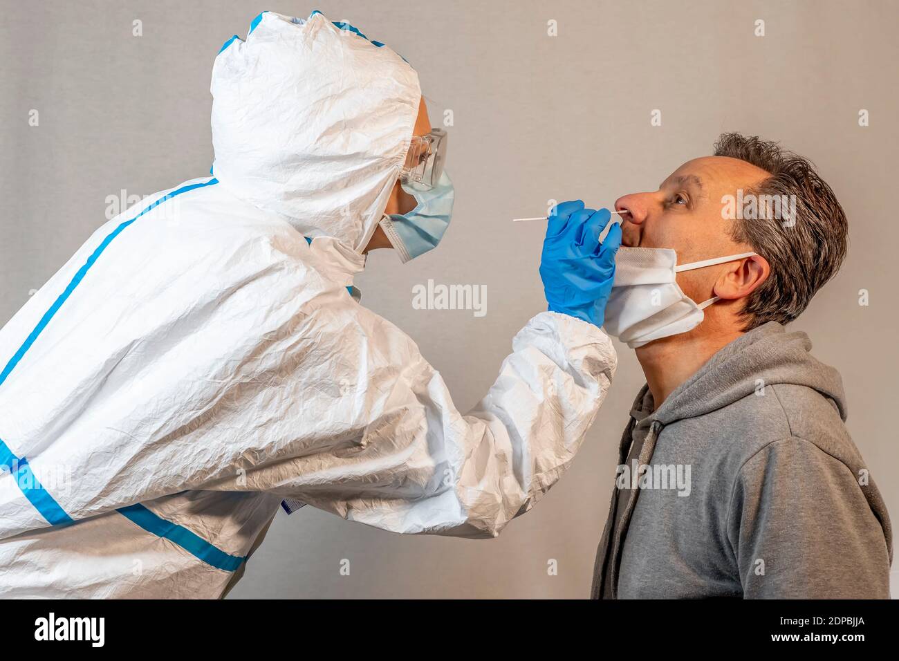 Ein Arzt, der vollständig mit einem weißen Overall, einer Schutzbrille, einer Maske und Handschuhen bedeckt ist, führt einem Patienten mittleren Alters einen Nasenabstrich für eine covid-19 che durch Stockfoto