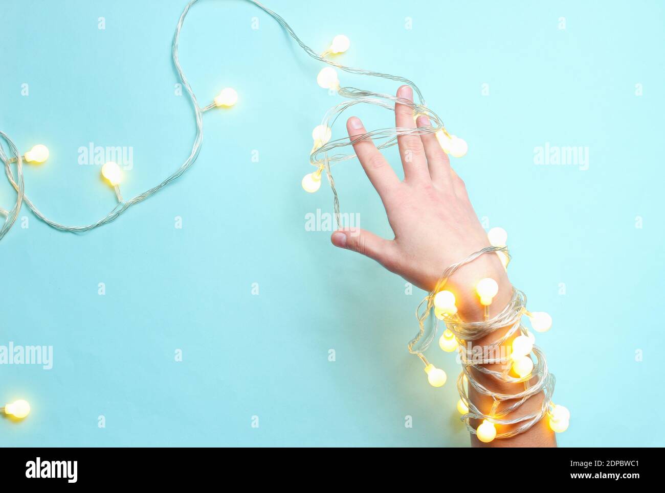 Minimalismus-Trend. Weibliche Hand mit hellen leuchtenden Girlanden von Glühbirnen auf blauem Hintergrund gewickelt. Draufsicht Stockfoto